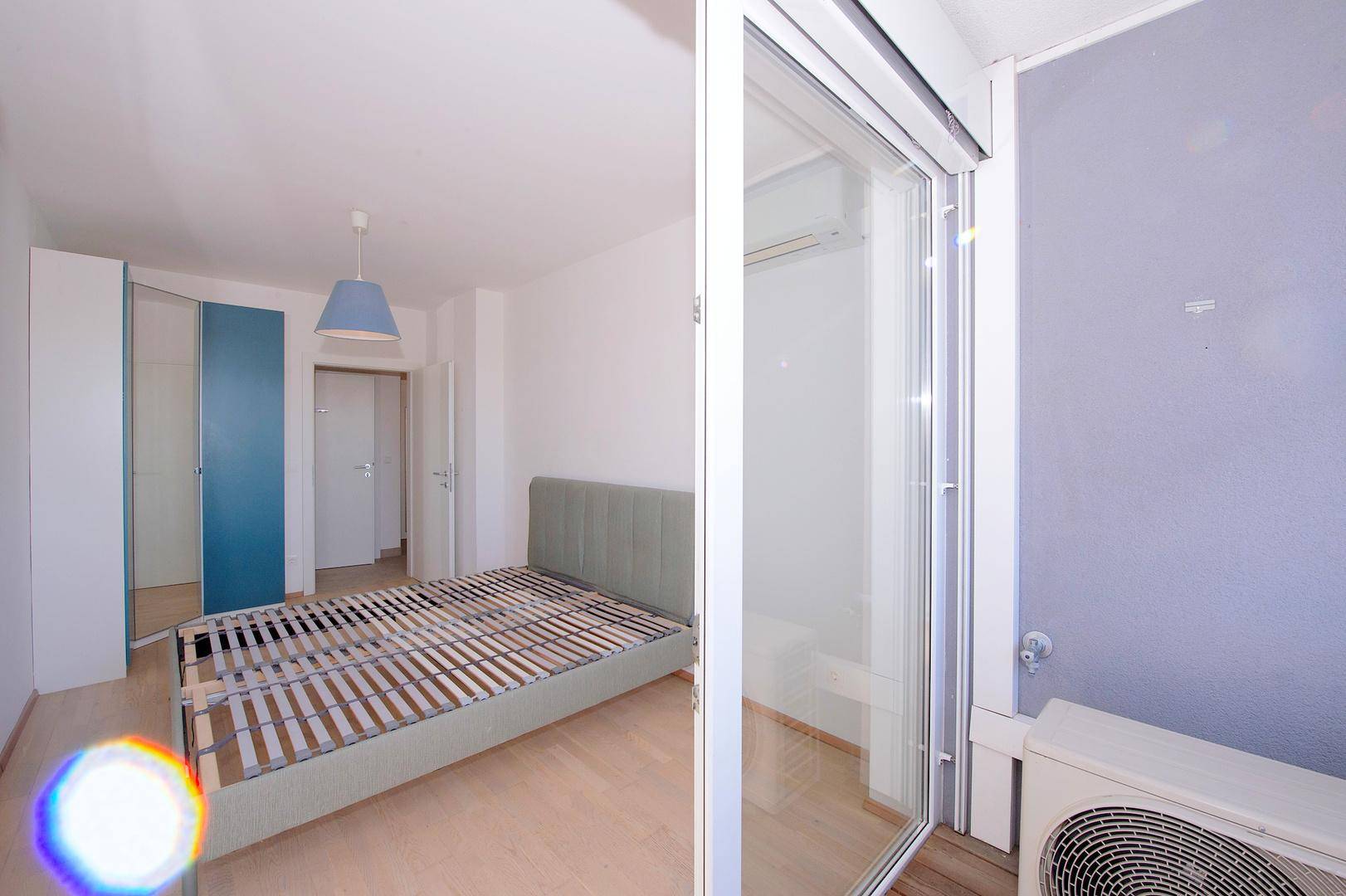 Helles Schlafzimmer mit Bettrahmen, Kleiderschrank und Zugang zum Balkon.