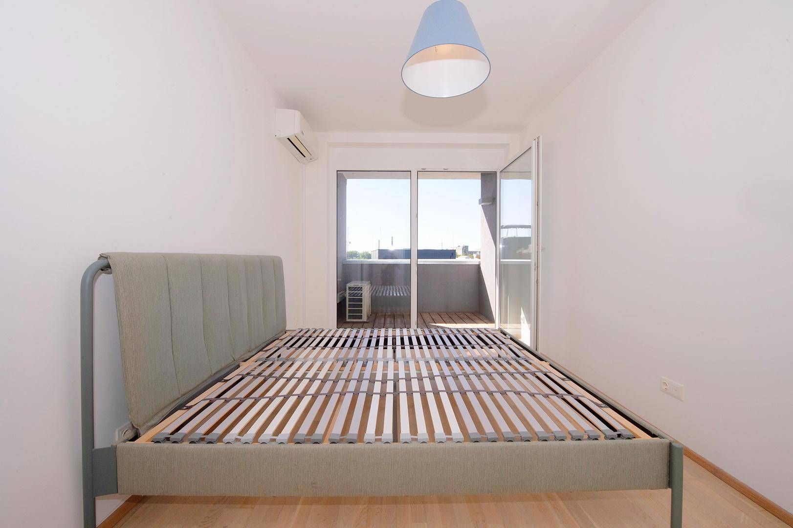 Helles Schlafzimmer mit Bettrahmen, Klimaanlage und direktem Zugang zum Balkon.