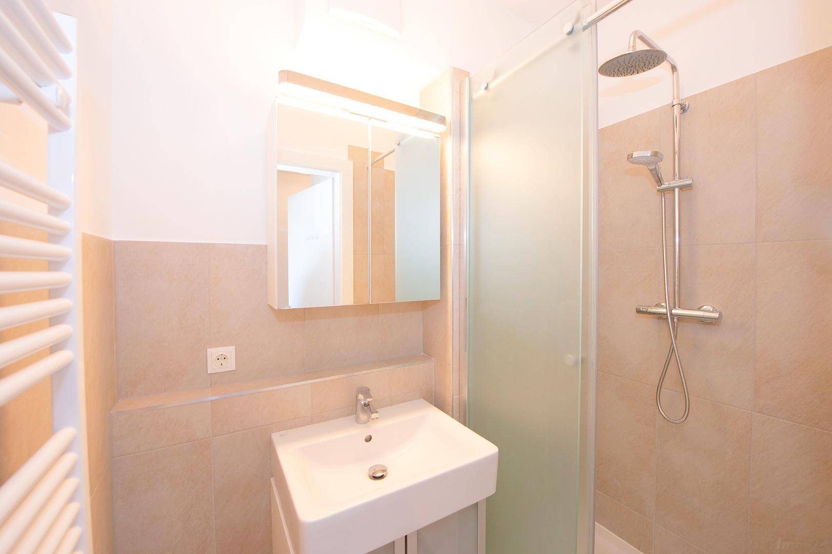 Helles Badezimmer mit Waschbecken, Spiegelschrank, Dusche und beheiztem Handtuchhalter.