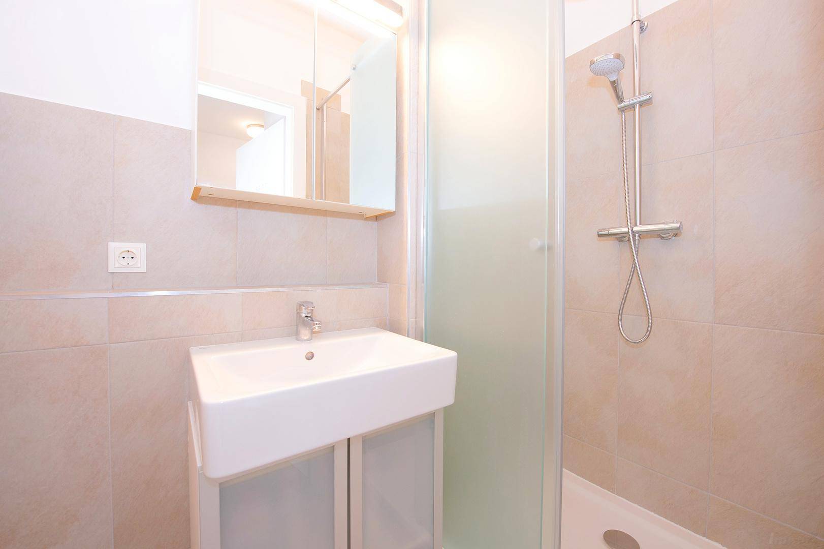 Modernes Badezimmer mit Waschbecken, Spiegelschrank und Duschkabine, hell gefliest.
