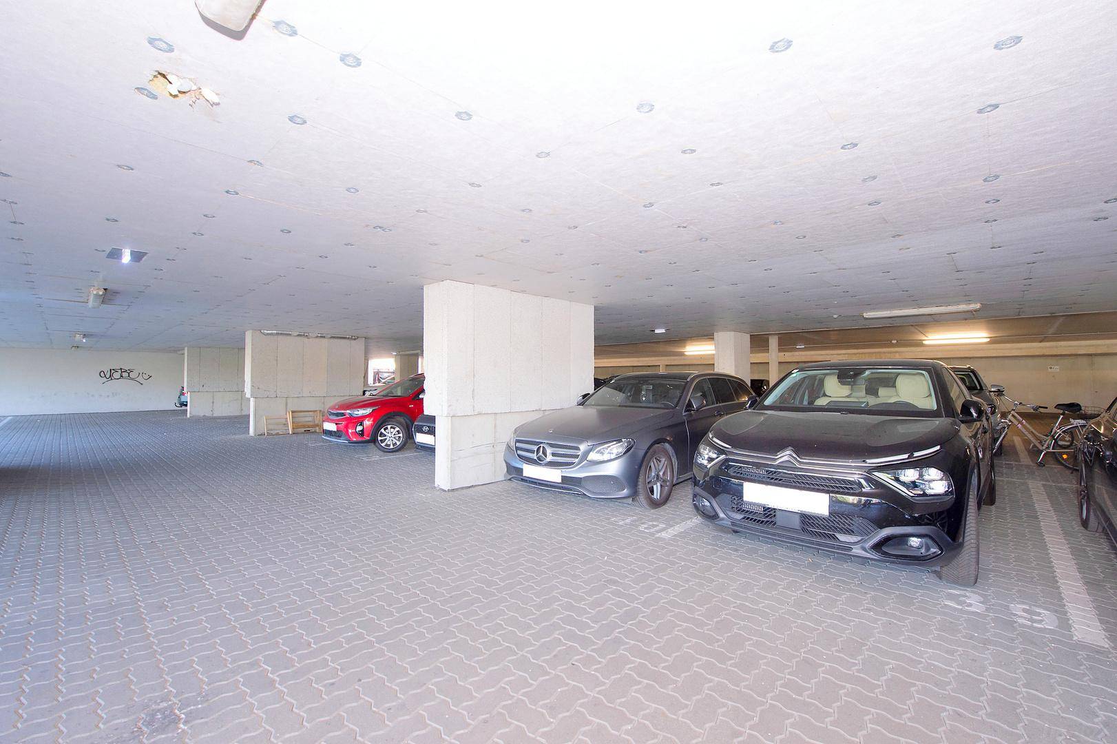 Geräumige Tiefgarage mit mehreren Stellplätzen und geparkten Fahrzeugen unter einer Betondecke.