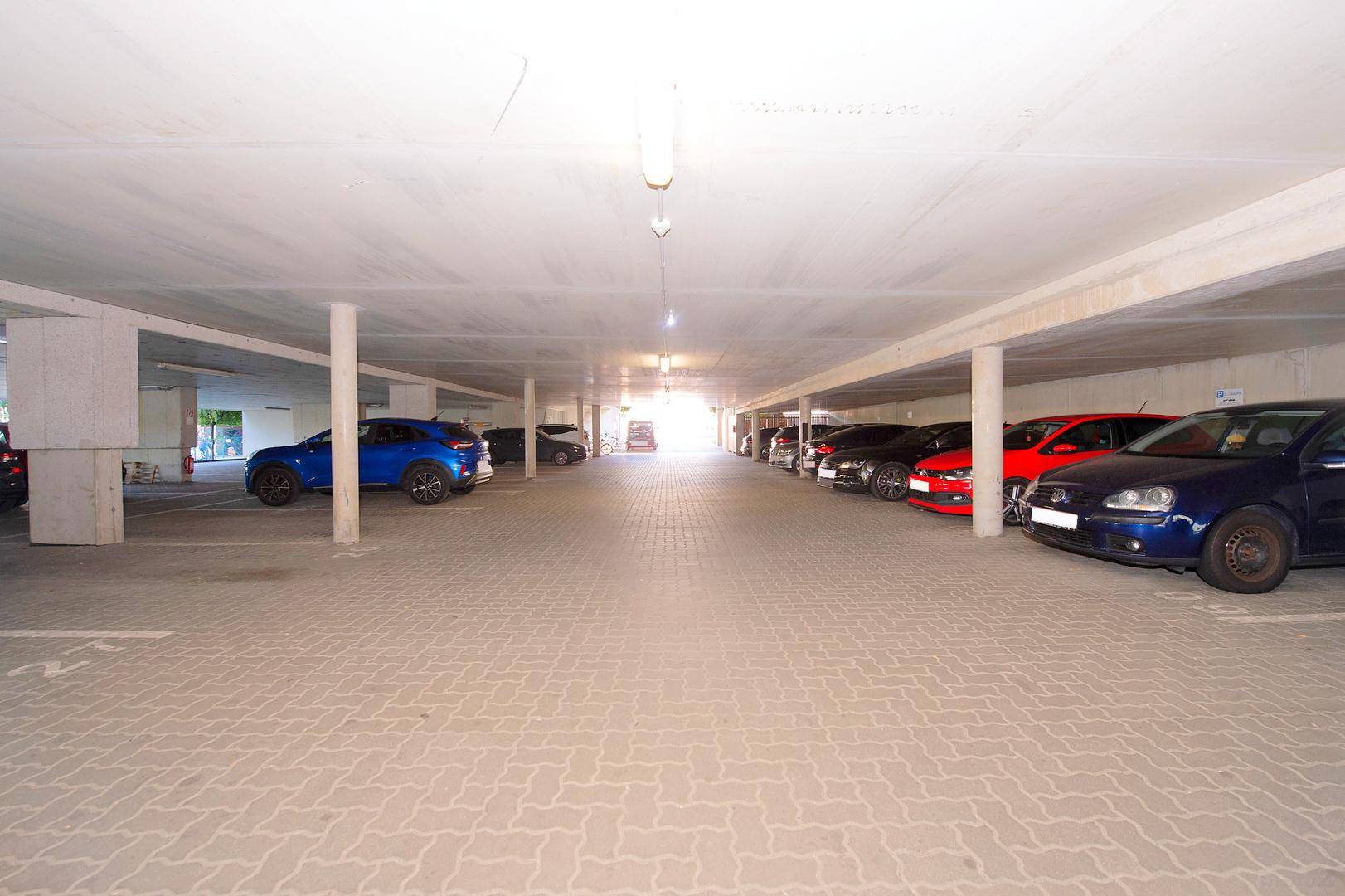 Lange Reihe von Parkplätzen in einer hell beleuchteten Tiefgarage mit vielen Fahrzeugen.