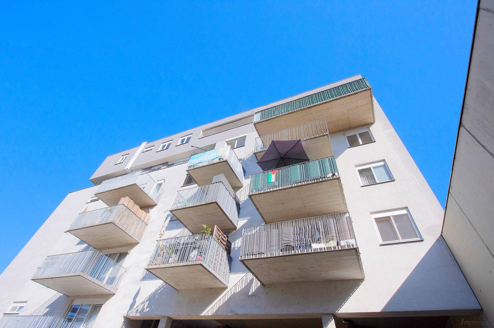 Gebäudefassade mit zahlreichen Balkonen, einige davon mit Sonnenschirmen und Dekorationen.