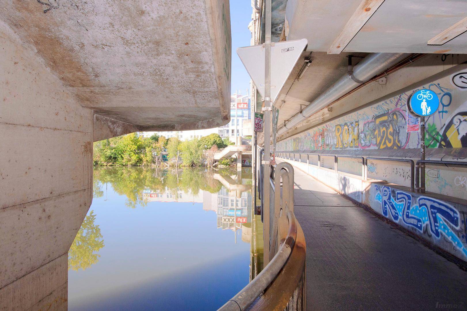 Blick unter einer Brücke hindurch auf den Fluss und die mit Graffiti verzierten Betonstrukturen.
