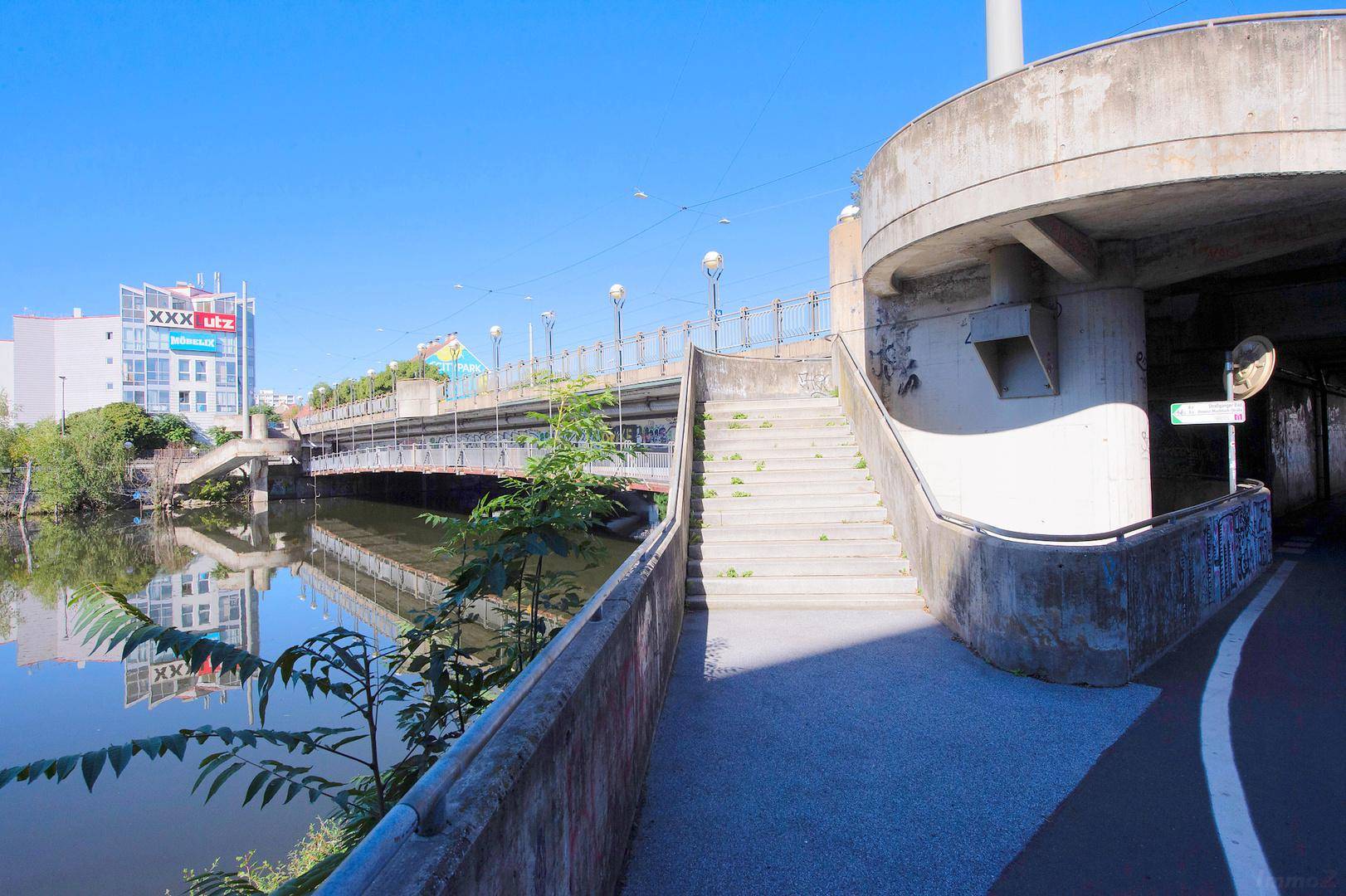 Brückenkonstruktion mit Treppenaufgang und dem Fluss darunter, umgeben von städtischer Architektur.