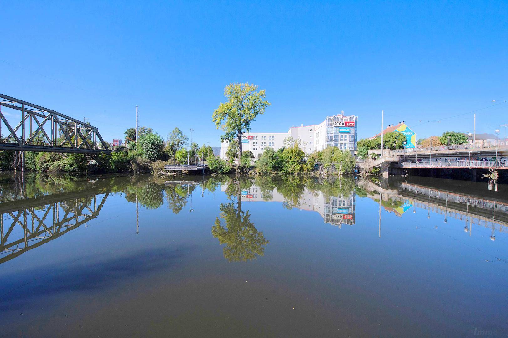 Panoramablick auf einen breiten Fluss mit Brücken und Gebäuden, die sich im Wasser spiegeln.