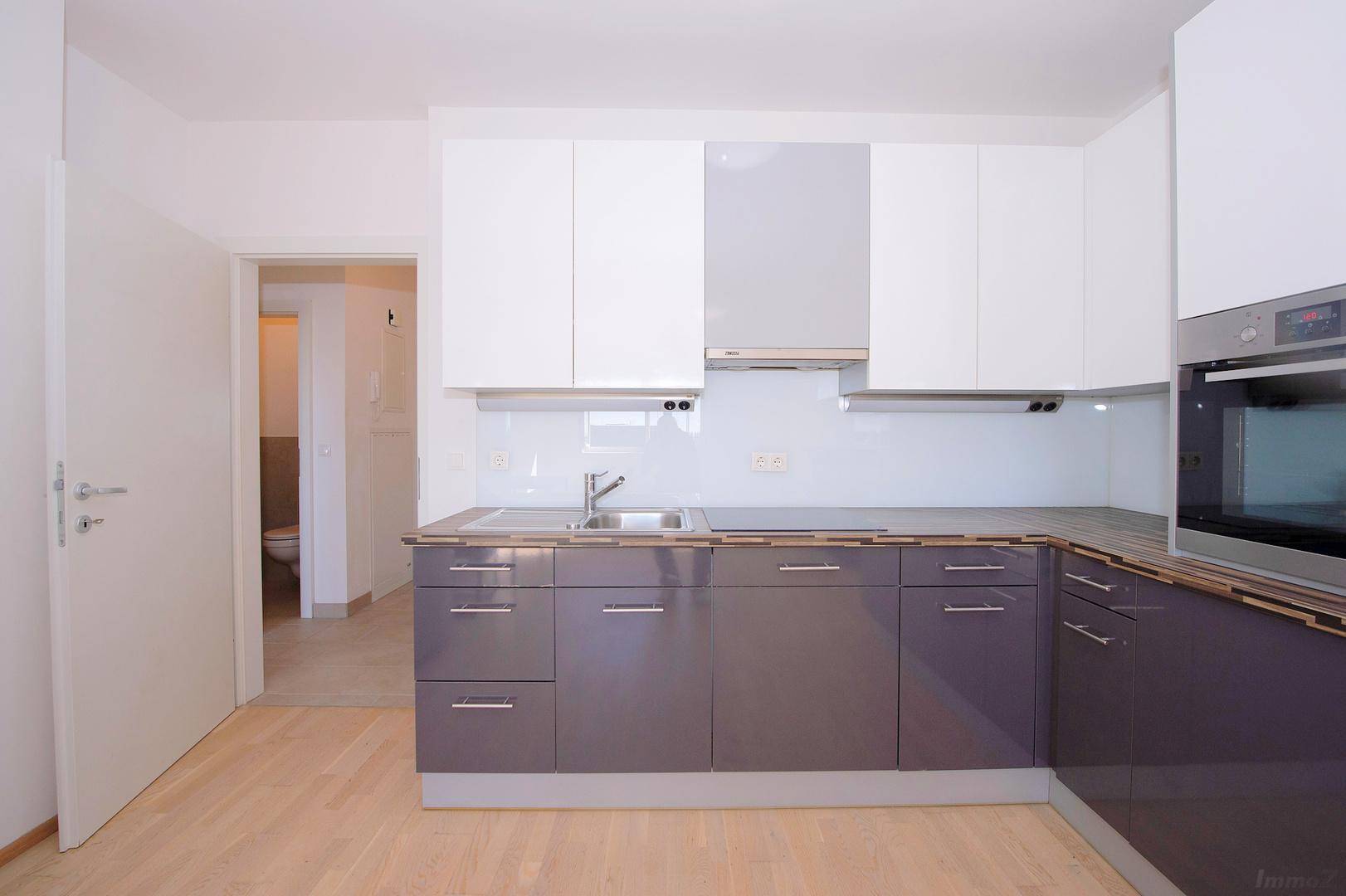 Moderne Einbauküche mit Spüle, Backofen und Zugang zu einem weiteren Raum.