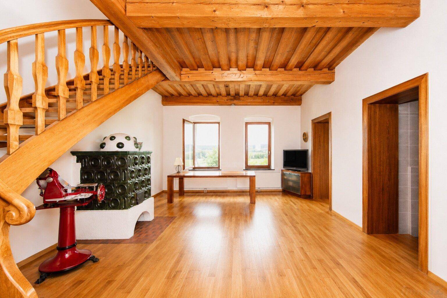 Geräumiges Wohnzimmer mit Holzbalkendecke, Kachelofen und geschwungener Holztreppe.