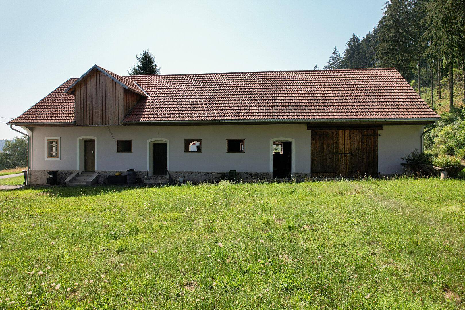 Langes Nebengebäude mit Ziegeldach und Holztüren in ländlicher Umgebung.