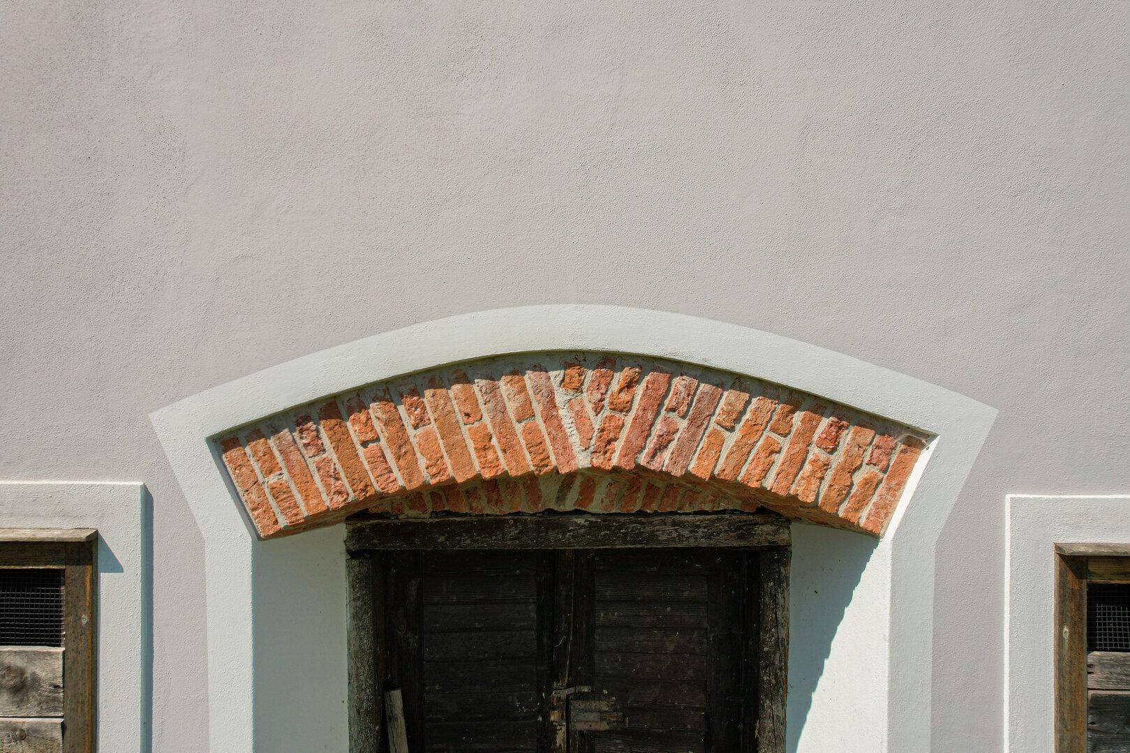 Detailansicht eines alten Ziegelbogens über einer Holztür an der Fassade.