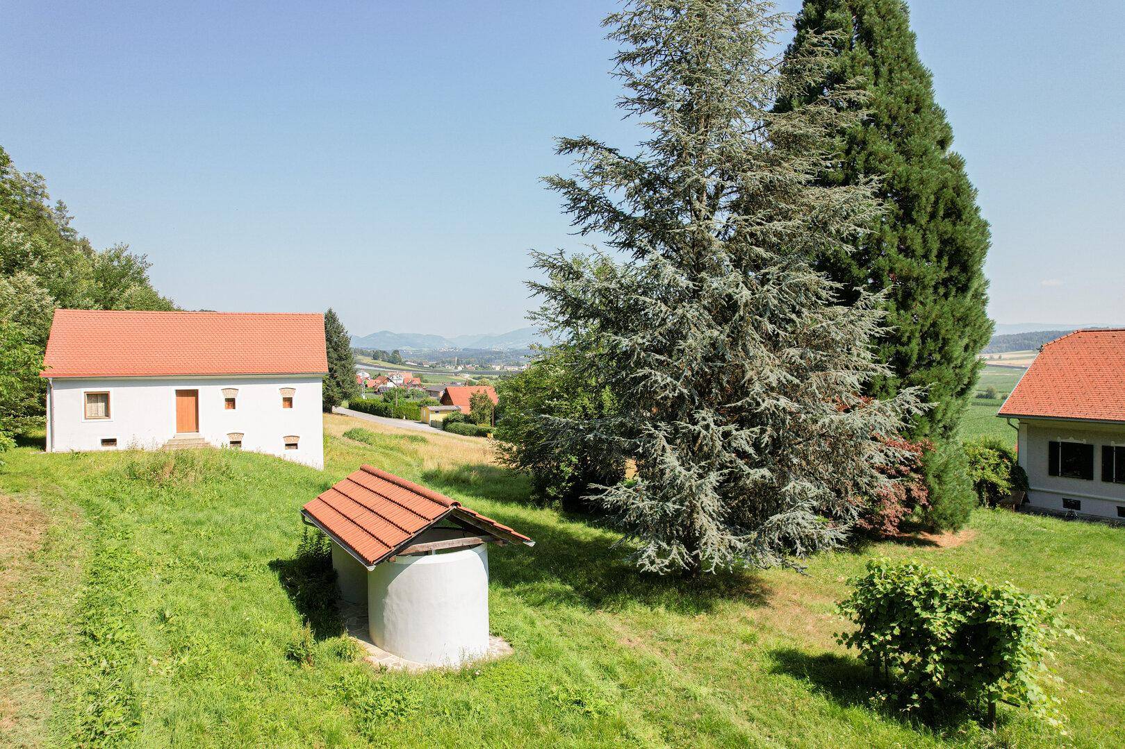 Weitläufige Landschaft mit mehreren Gebäuden, Bäumen und einem kleinen Brunnenhaus.