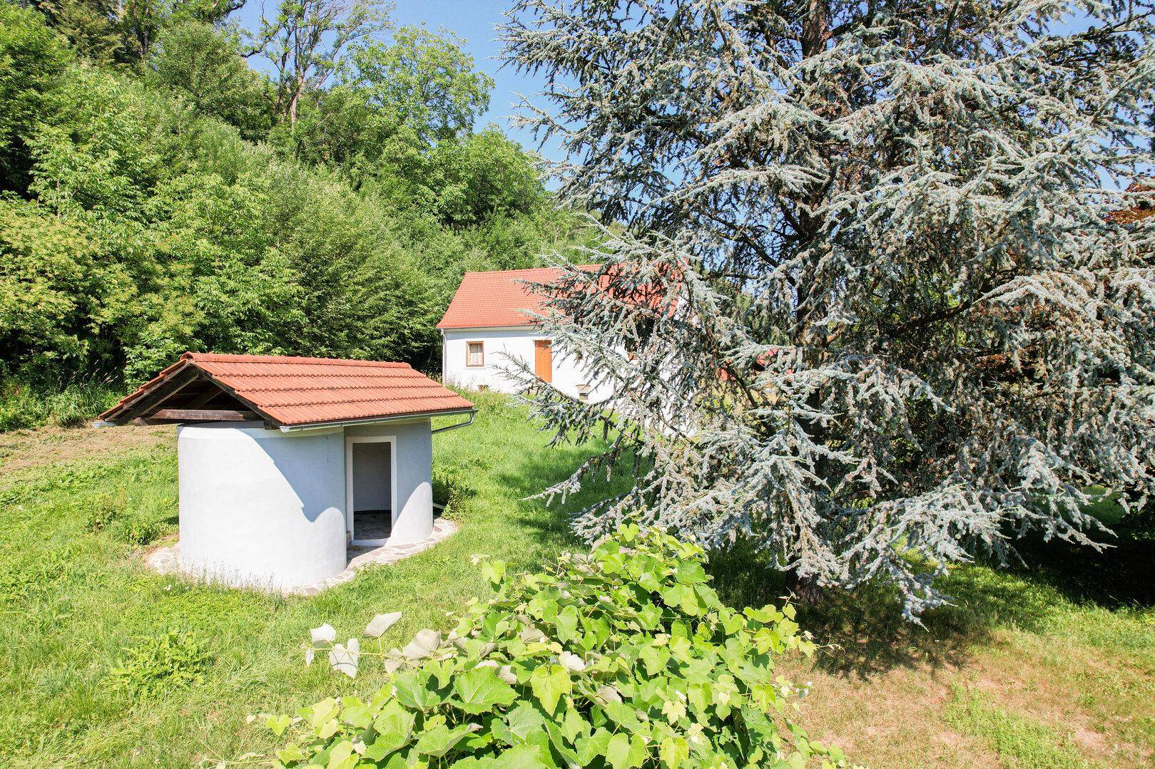 Kleines Brunnenhaus mit Ziegeldach und umgebender Vegetation in ländlicher Umgebung.