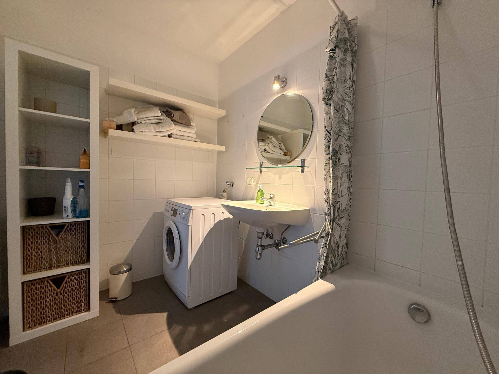 Funktionales Badezimmer mit Badewanne, Waschbecken, Waschmaschine und praktischen Ablagen.