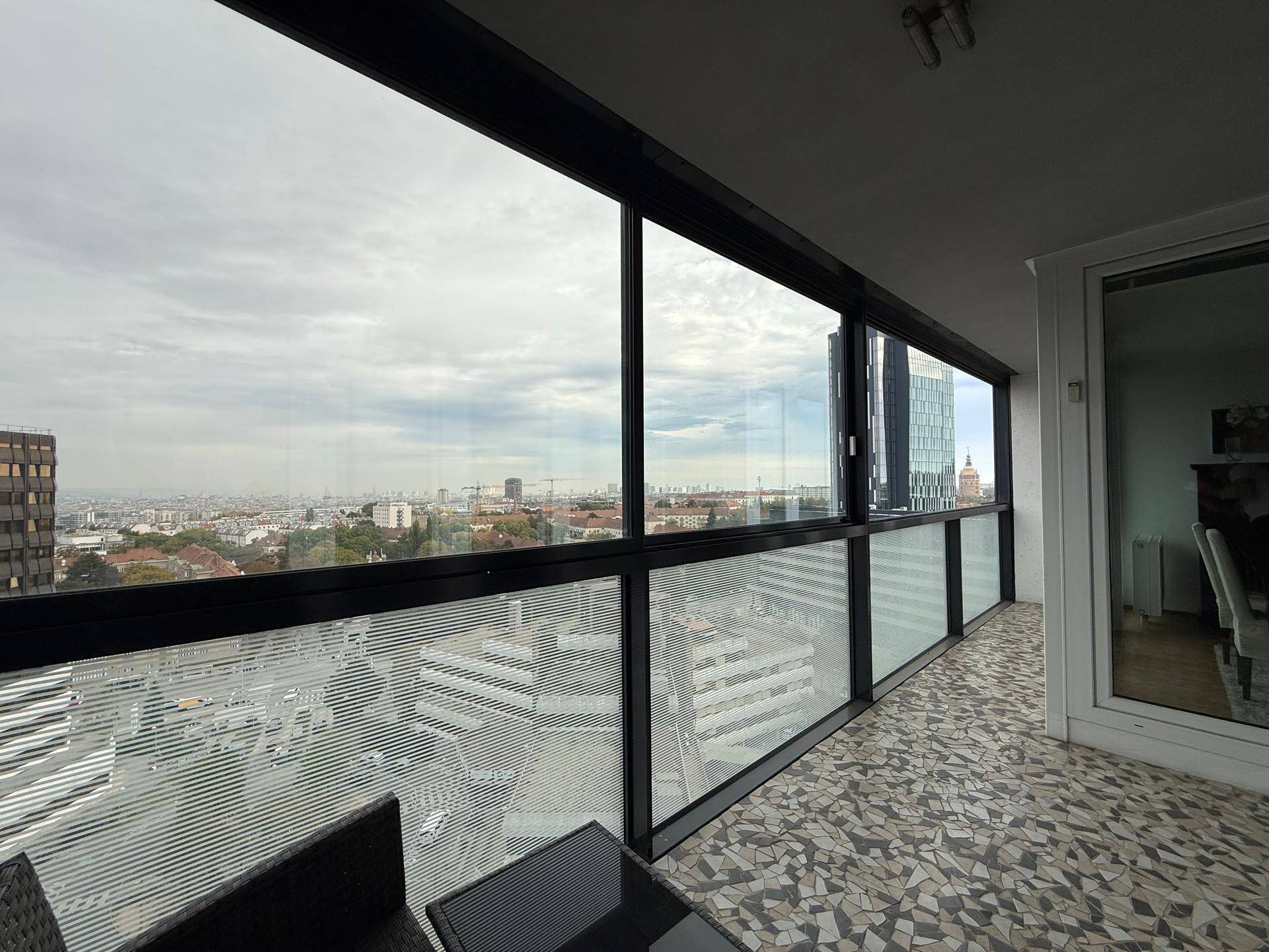 Verglaste Loggia mit bequemen Sitzmöbeln und weitem Panoramablick über die Stadt.