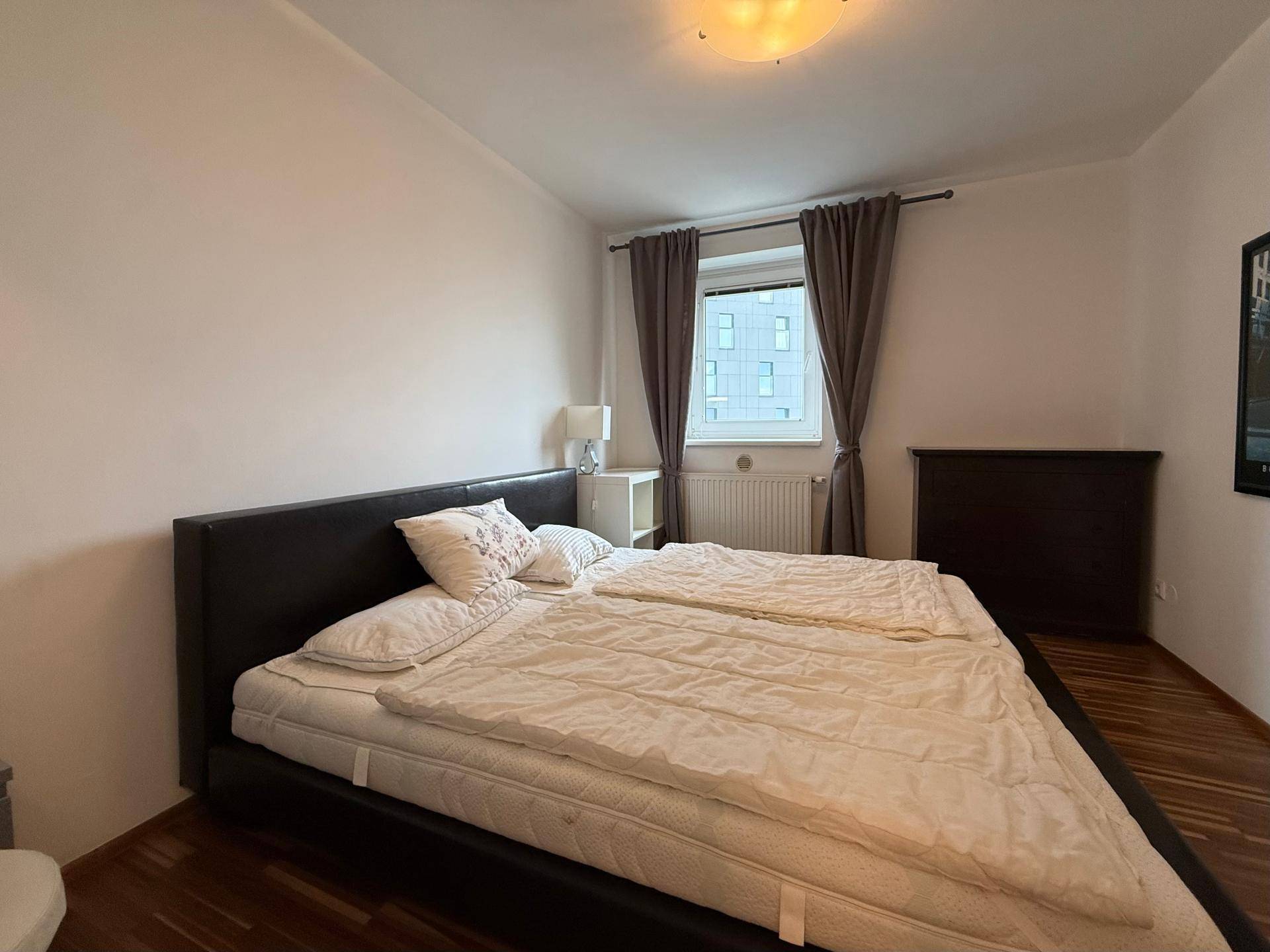 Gemütliches Schlafzimmer mit großem Doppelbett, Holzboden und einem Fenster mit Blick auf Gebäude.