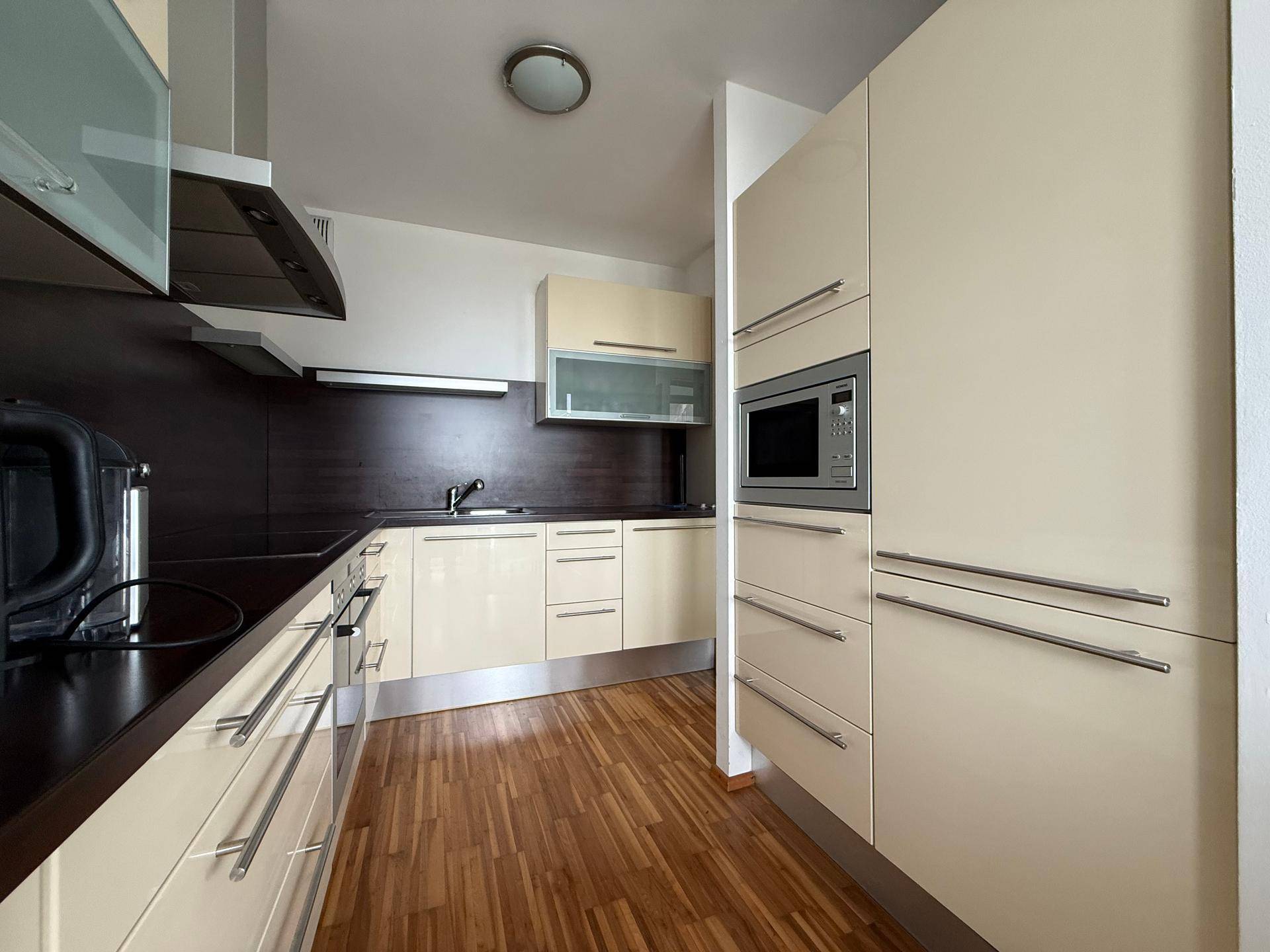 Moderne Einbauküche mit beigen Hochglanzfronten, dunklen Arbeitsplatten und integrierten Geräten.