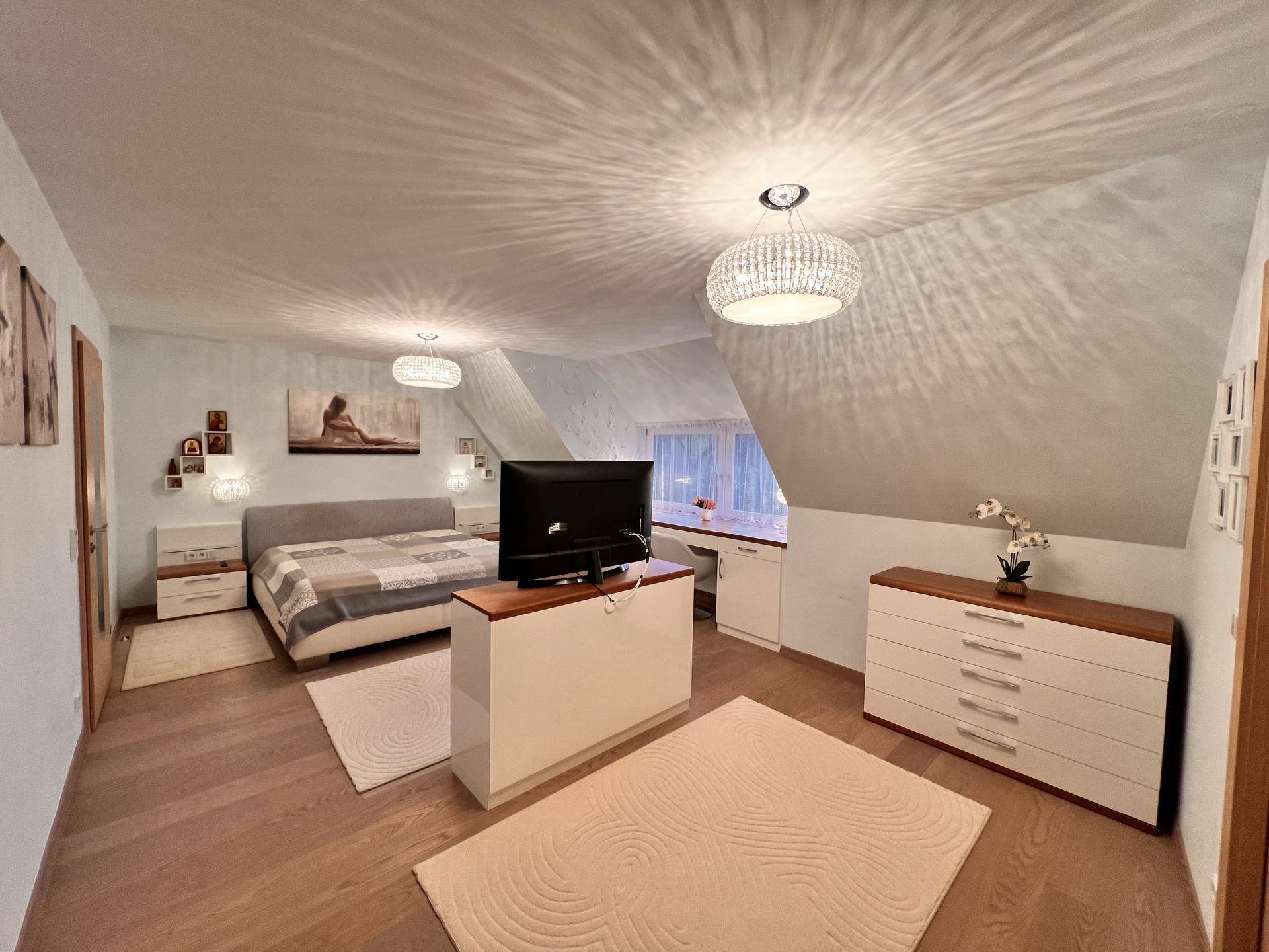 Gemütliches Schlafzimmer im Dachgeschoss mit Holzboden, schrägen Wänden und moderner Einrichtung.