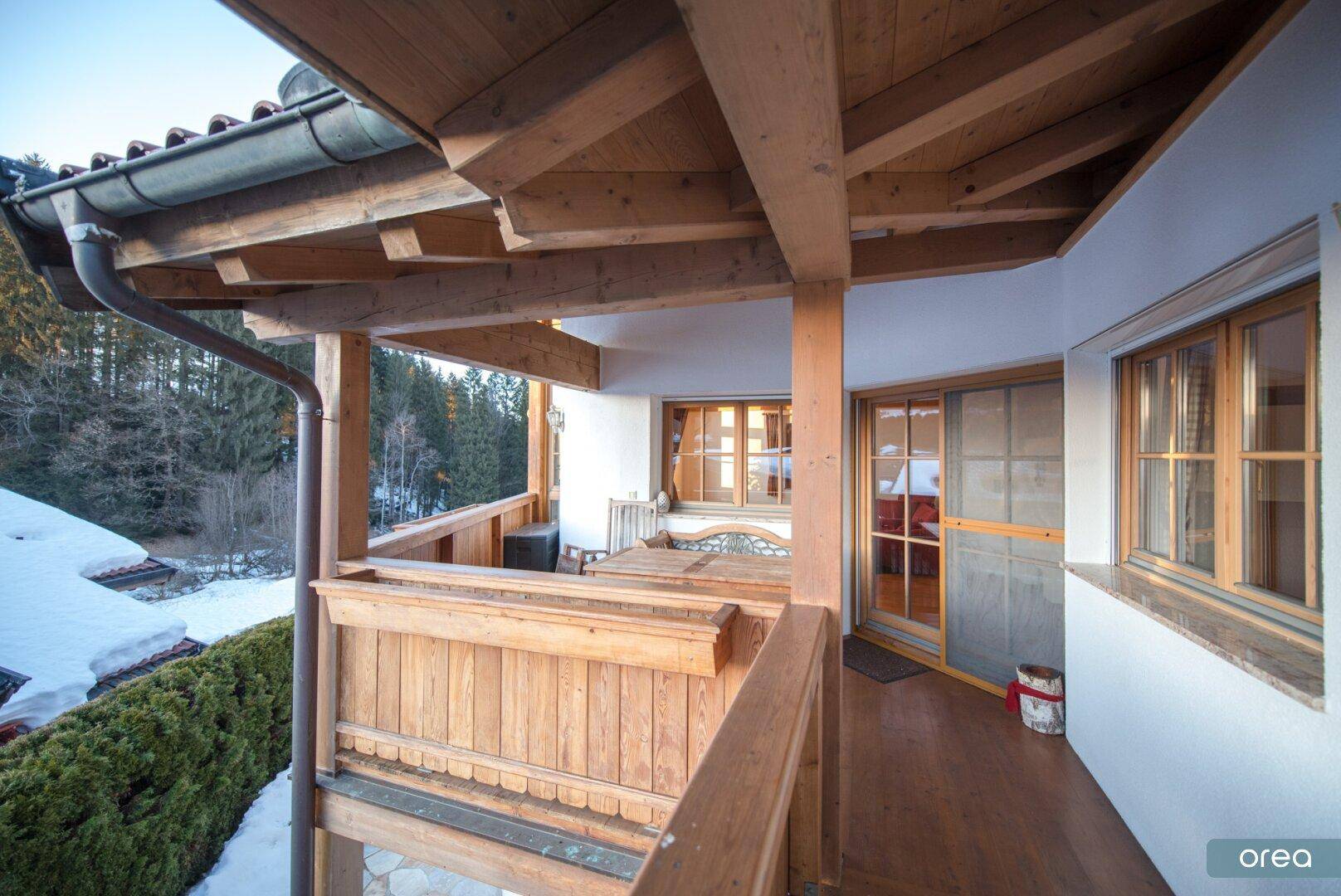 Überdachter Holzbalkon mit Blick auf die verschneite Landschaft und angrenzende Wälder.
