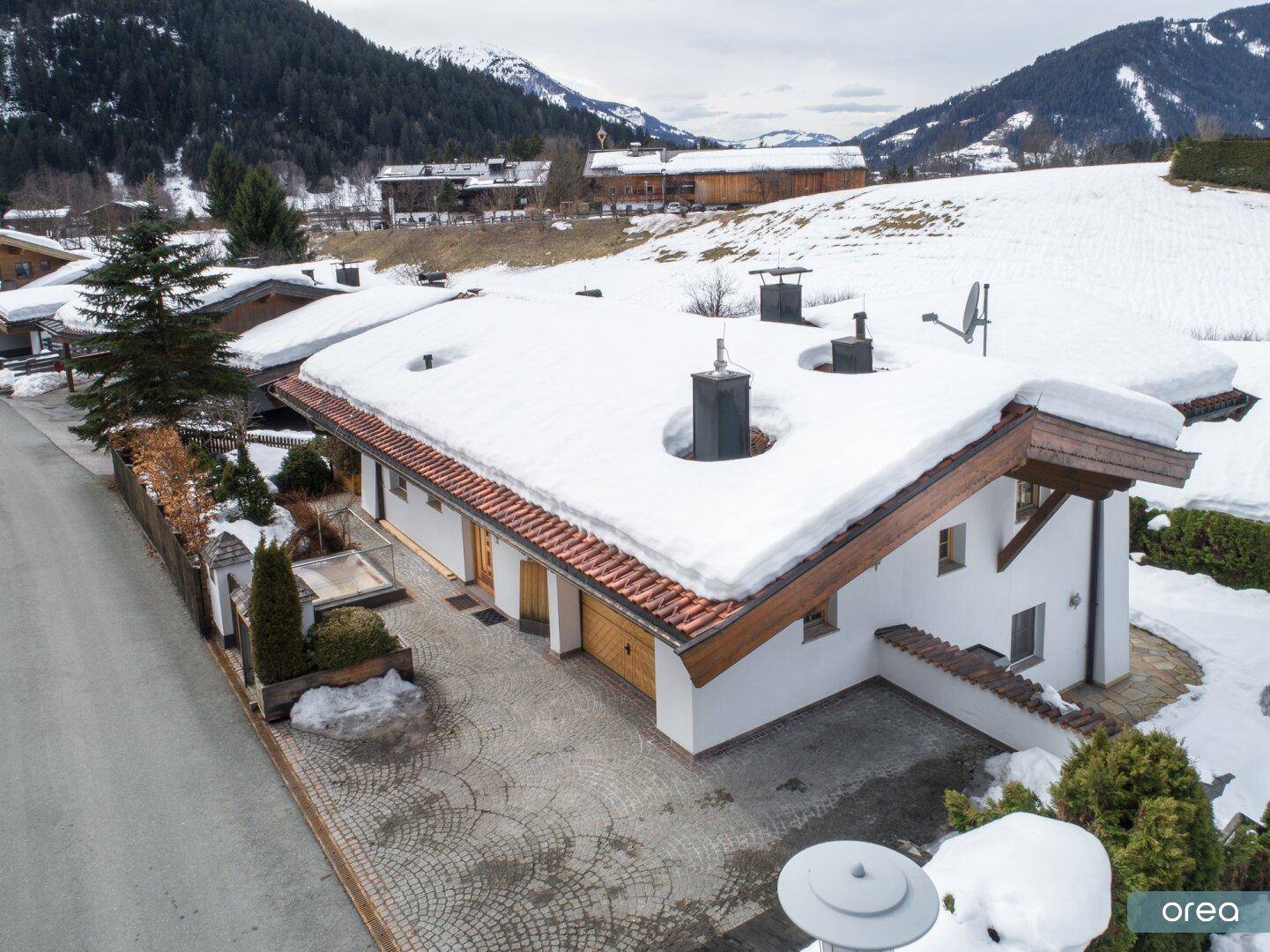 Dachansicht des Chalets mit verschneitem Ziegeldach und gepflasterter Zufahrt im Winter.