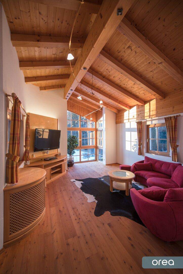 Gemütliches Wohnzimmer im Chalet-Stil mit Holzbalkendecke, großen Fenstern und rotem Sofa.