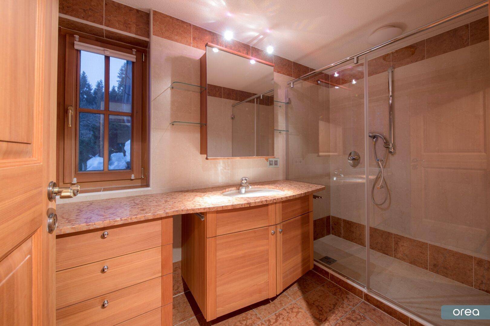 Modernes Badezimmer mit Dusche, Waschtisch und Fenster mit Blick ins Grüne.