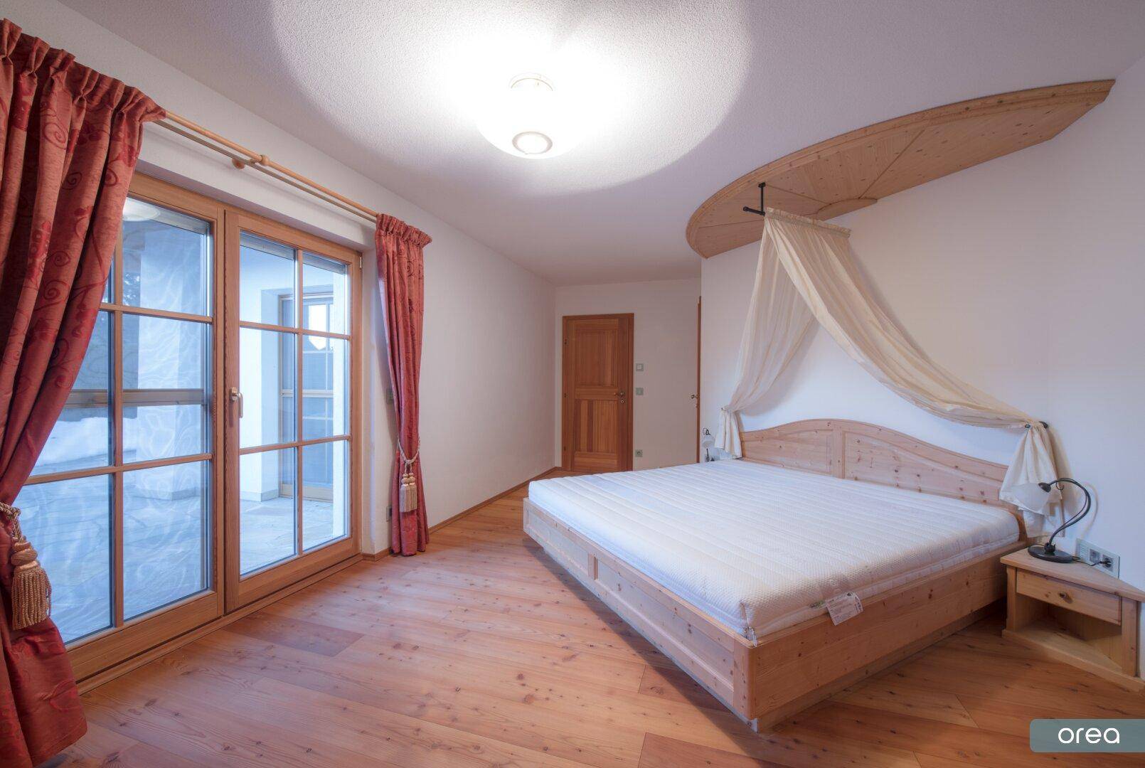 Gemütliches Schlafzimmer mit Holzbett, Parkettboden und Zugang zum Balkon.