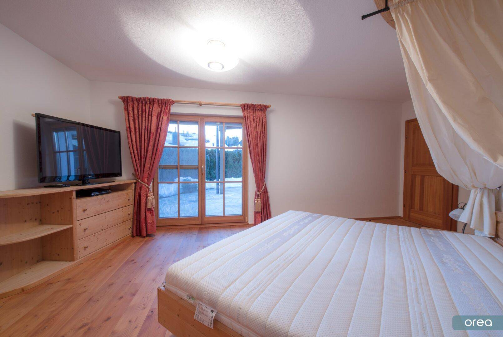 Helles Schlafzimmer mit Holzboden, Fernseher und Blick auf die verschneite Landschaft.