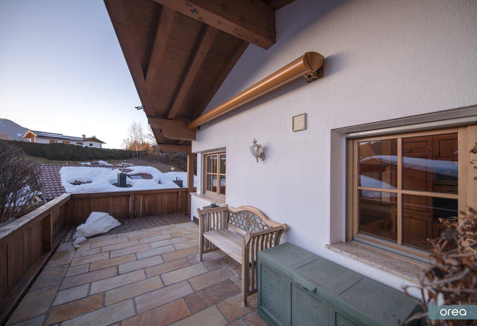 Gepflasterte Terrasse mit Holzsitzbank und Blick auf die verschneite Umgebung des Chalets.