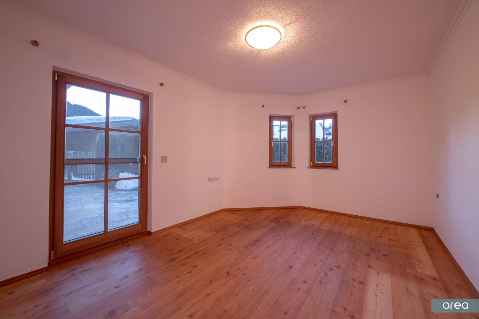 Leeres Zimmer mit Holzboden und Zugang zu einem Außenbereich, ideal als Schlafzimmer.