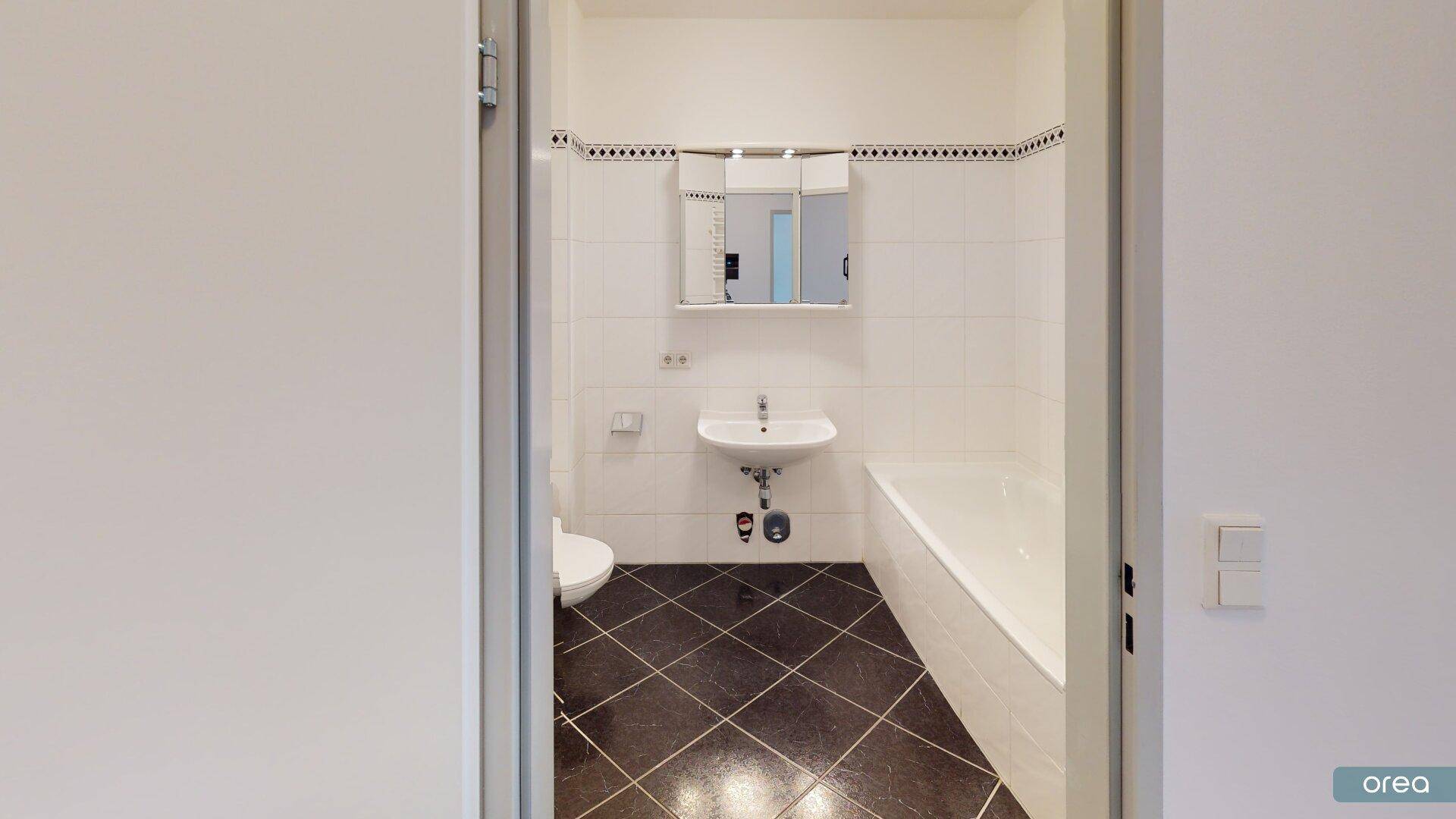 Modernes Badezimmer mit Badewanne, Waschbecken und WC, ausgestattet mit dunklen Bodenfliesen.