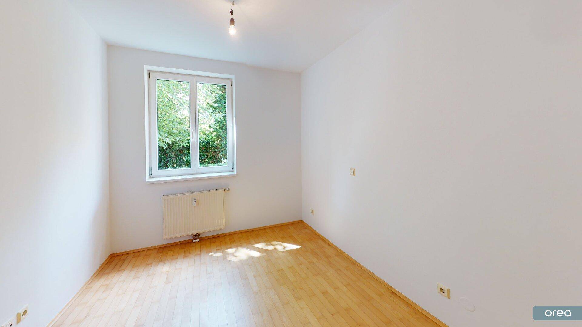 Helles Schlafzimmer mit Parkettboden und Fenster mit Blick ins Grüne.