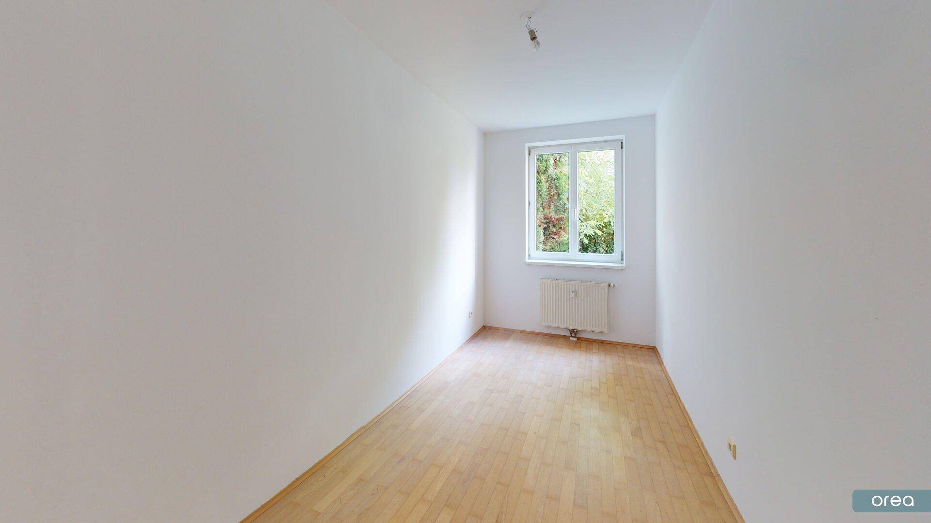 Geräumiges Zimmer mit hellem Parkettboden und Fenster, das viel Tageslicht hereinlässt.