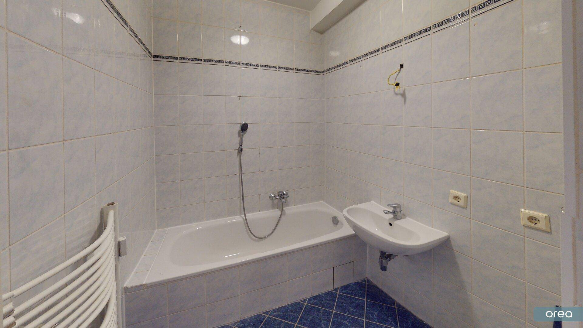 Badezimmer mit hellblauen Fliesen, Badewanne mit Duschfunktion und beheiztem Handtuchhalter.