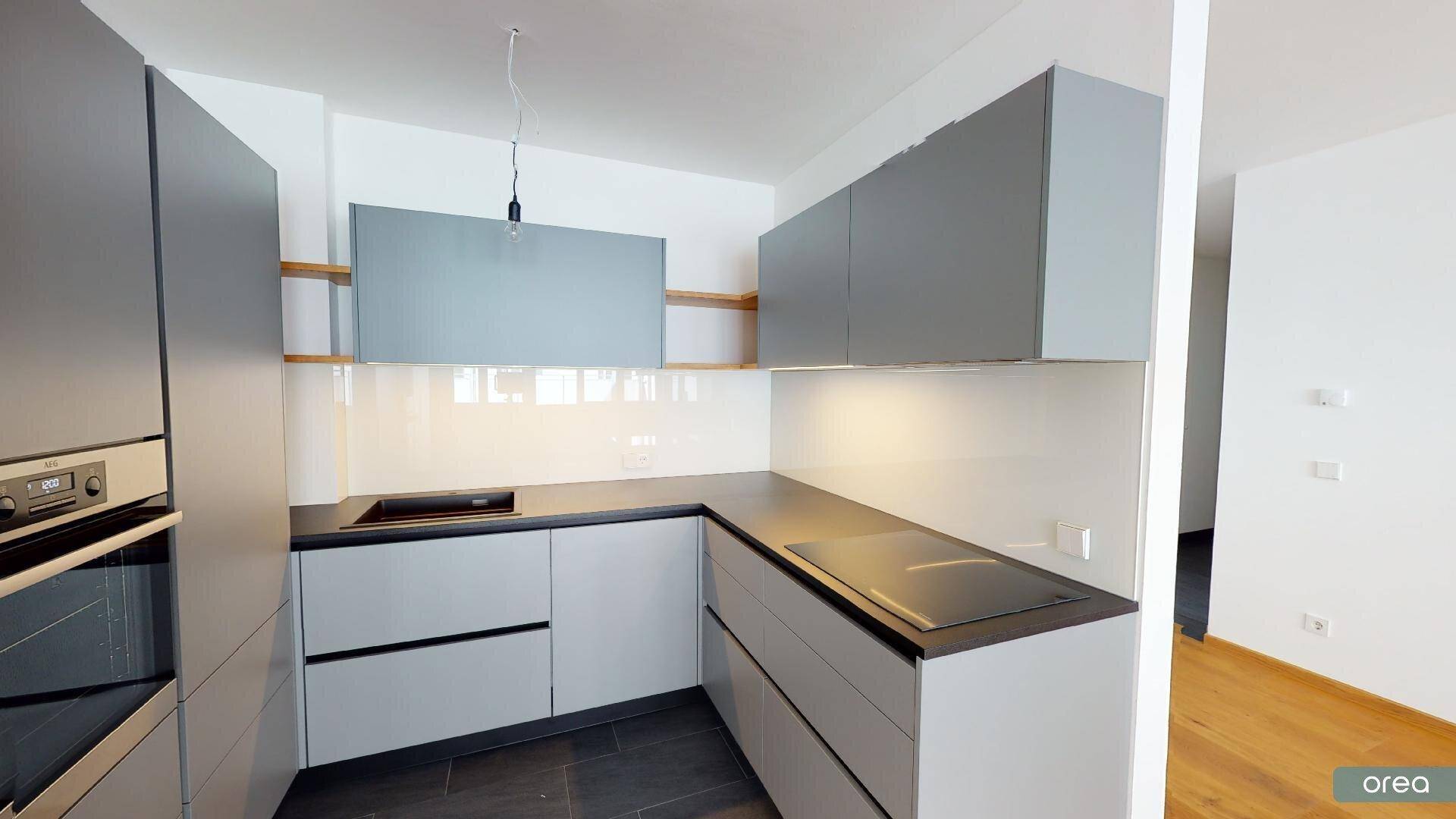 Moderne Einbauküche mit grauen Schränken, Induktionskochfeld und integriertem Backofen.