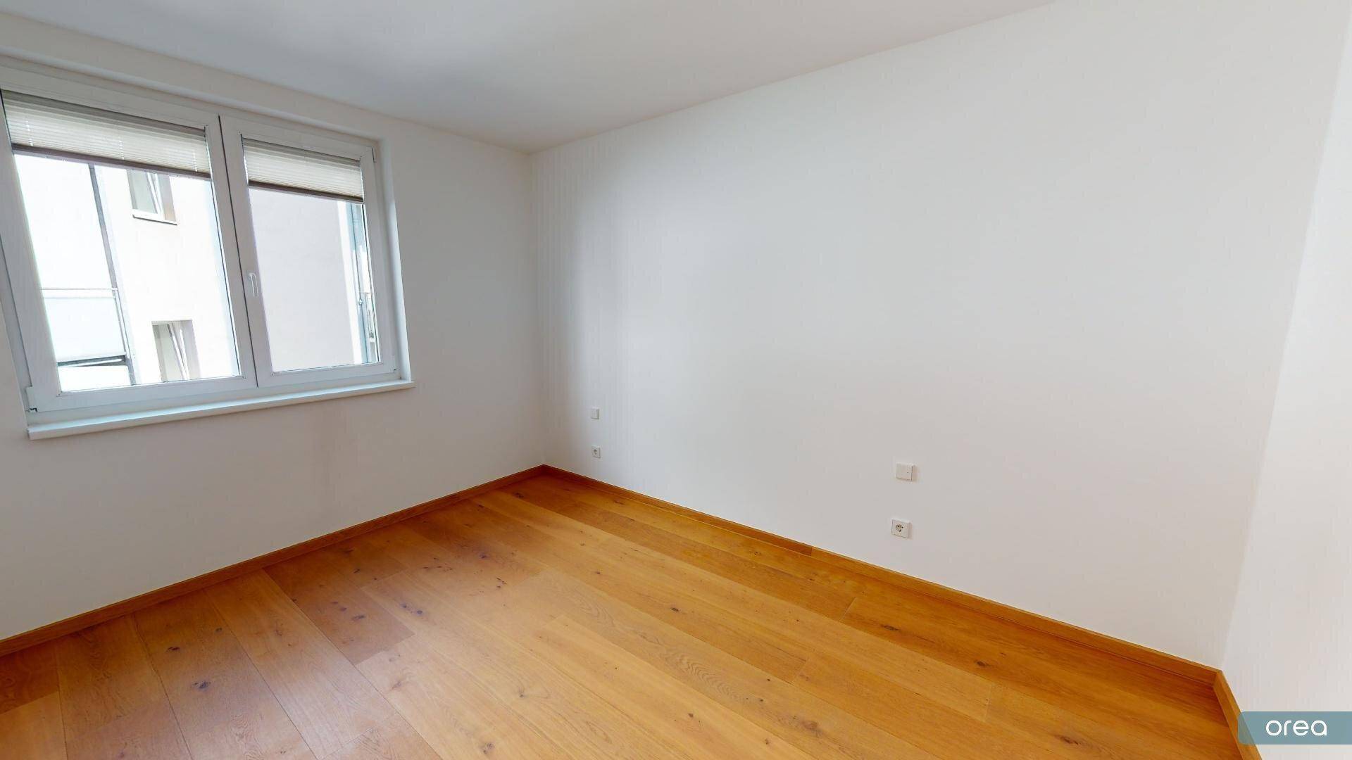 Helles Schlafzimmer mit Parkettboden und Fenster, bereit zur individuellen Gestaltung.