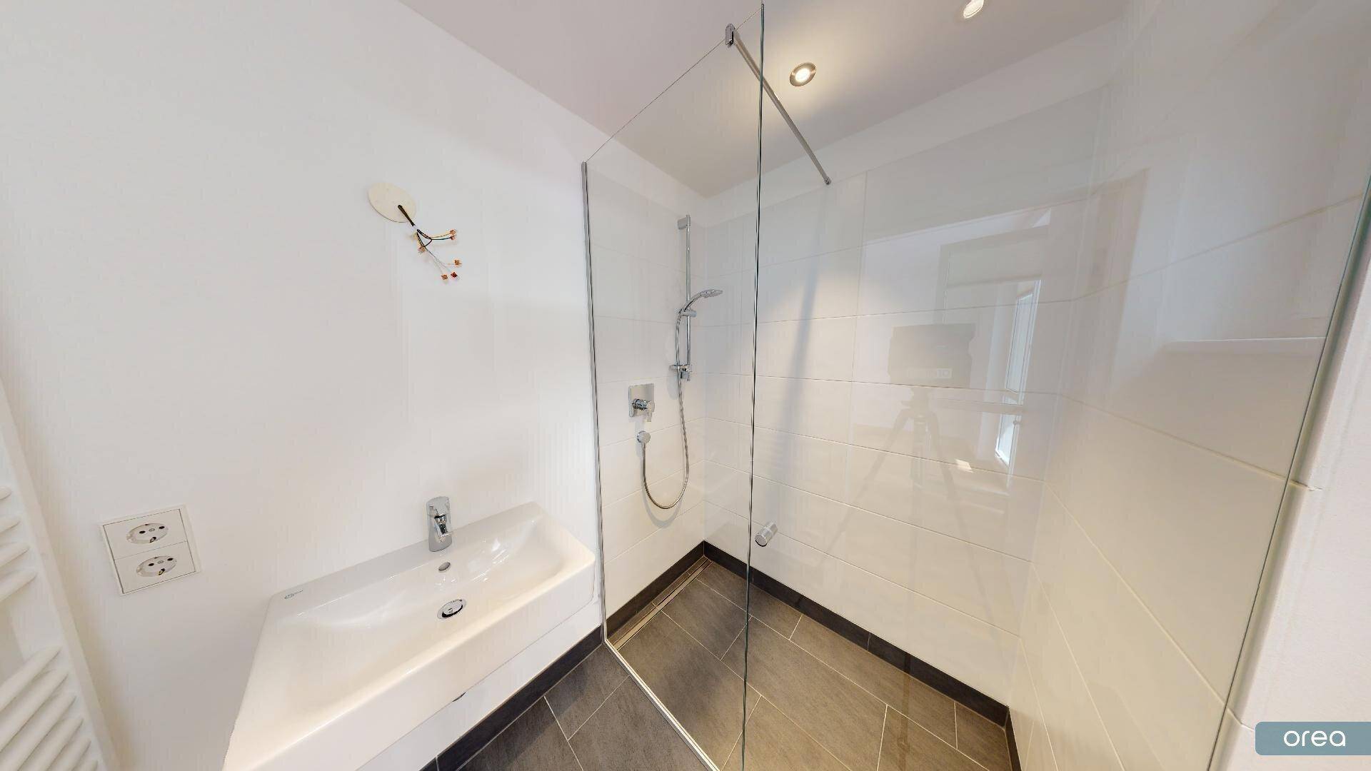 Helles Badezimmer mit moderner ebenerdiger Dusche, Waschbecken und Handtuchheizkörper.