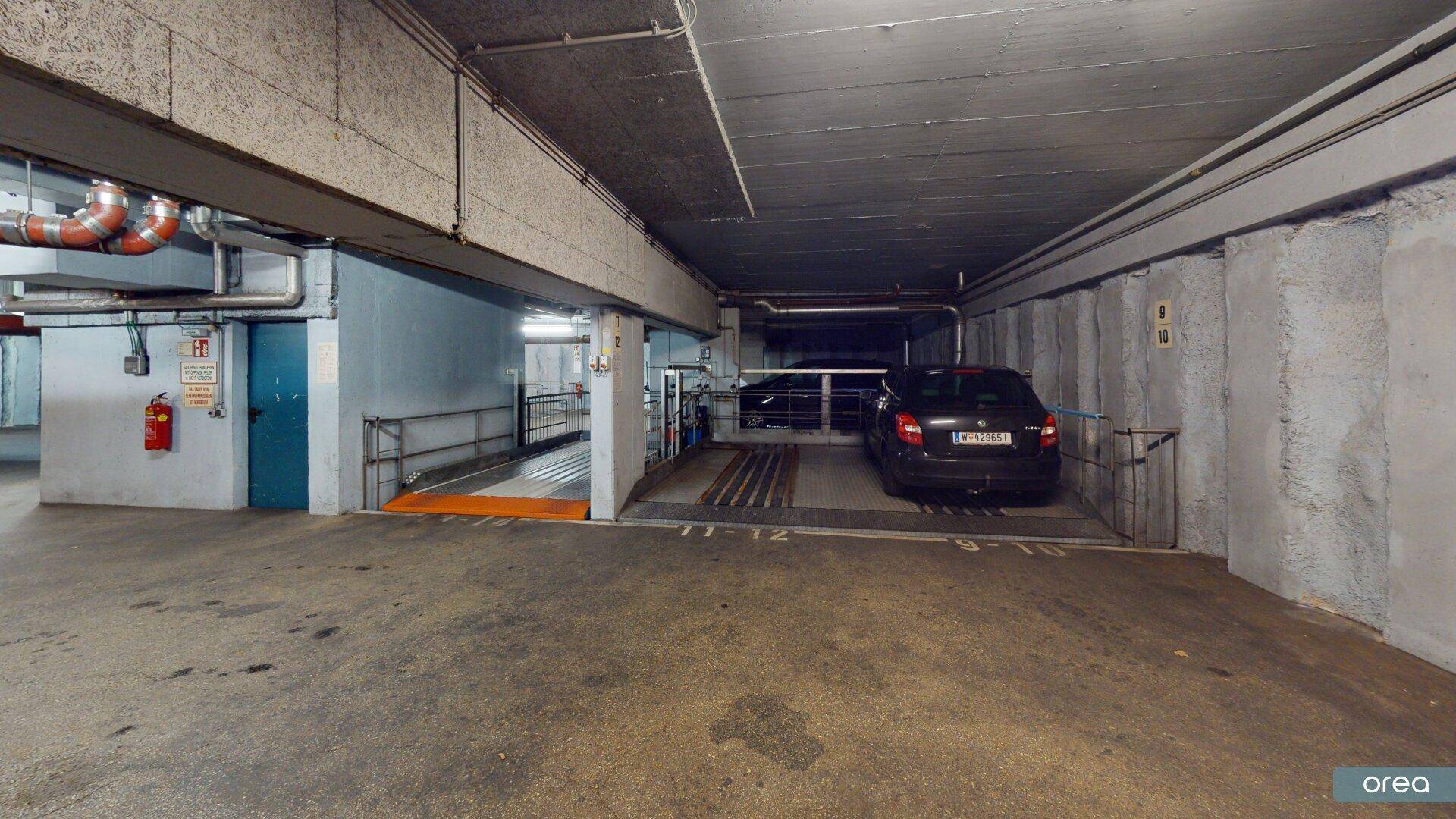 Tiefgarage mit Fahrzeugstellplätzen und Zugang zu weiteren Ebenen über eine mechanische Rampe.