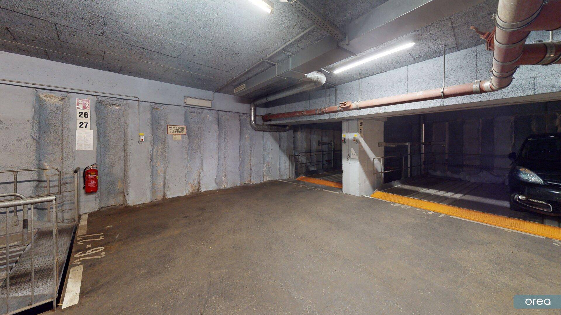 Ecke der Tiefgarage mit Betonwänden, Brandschutzvorrichtung und Zugang zur Parkrampe.