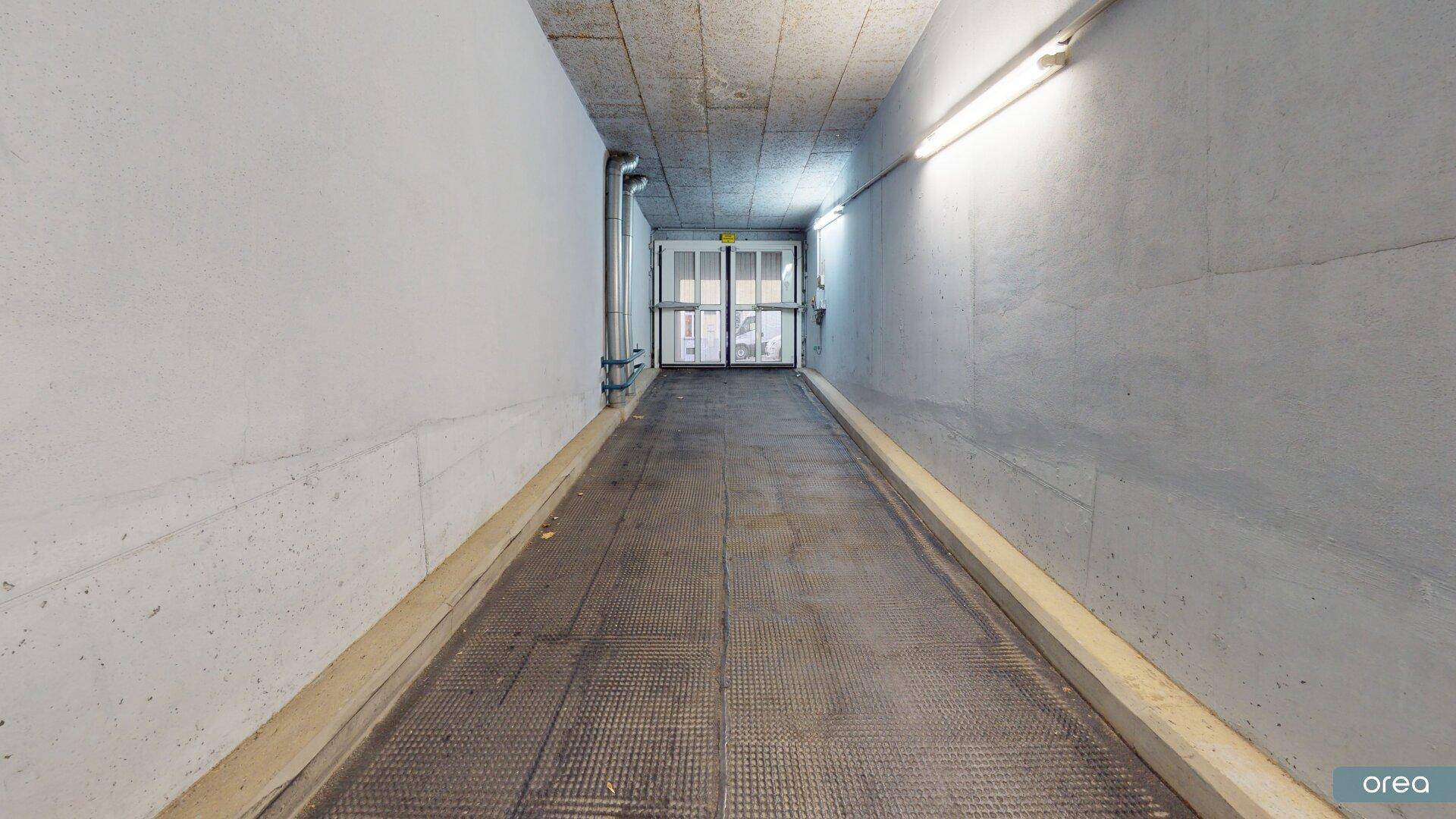 Ausfahrt der Tiefgarage mit langer Rampe, Betonelementen und einer Tür am Ende des Ganges.