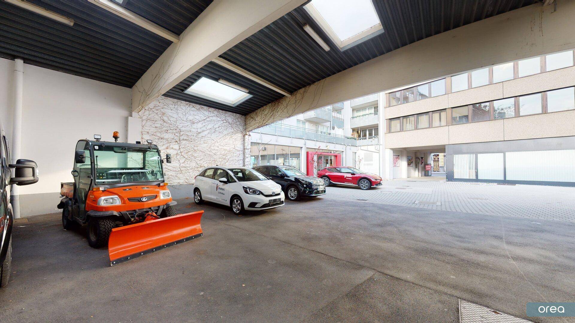 Überdachter Außenbereich mit Parkplätzen und Blick auf die moderne Gebäudefassade.