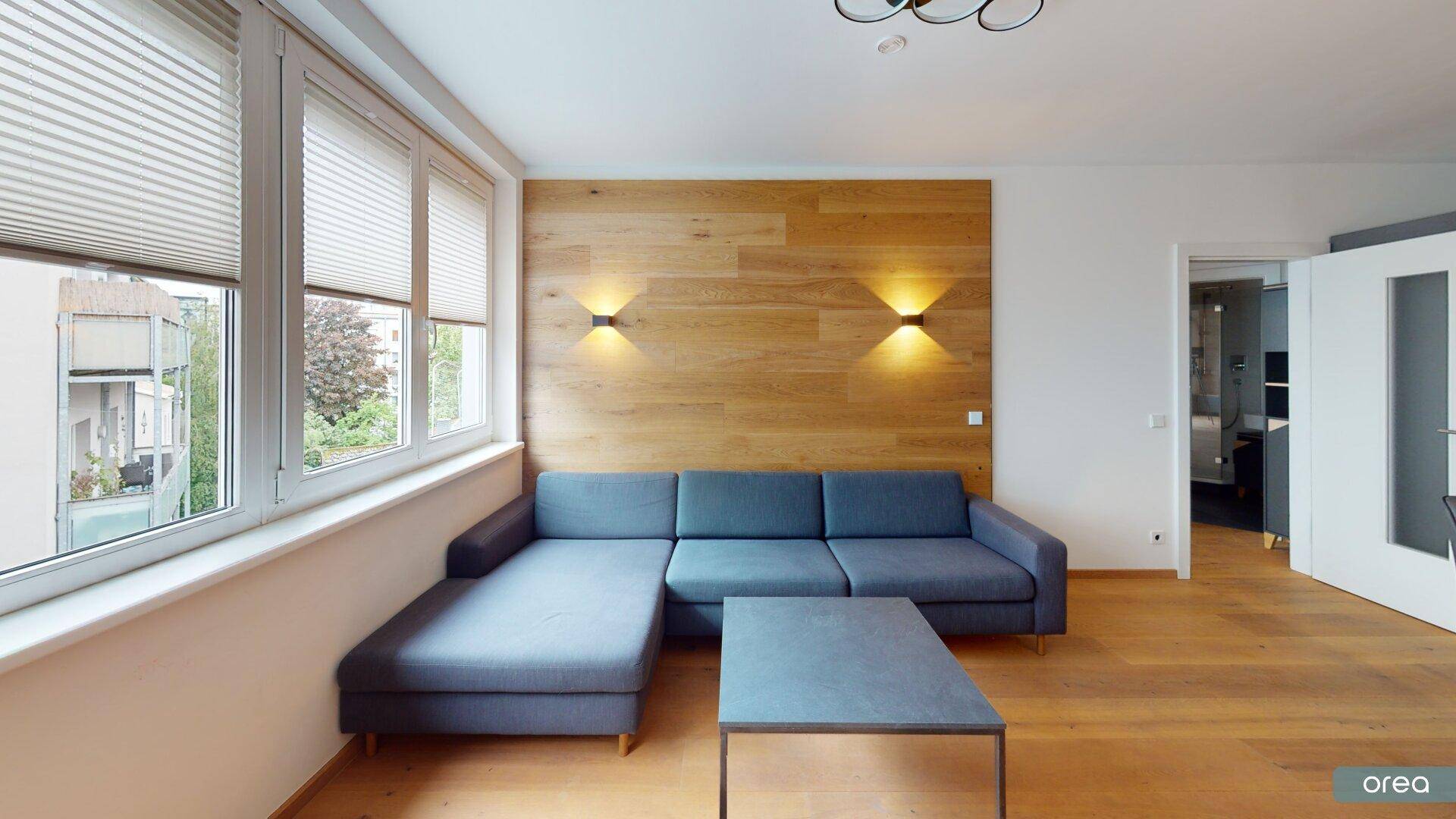 Gemütliches Wohnzimmer mit bequemer Couch, Holzwandverkleidung und viel Tageslicht.
