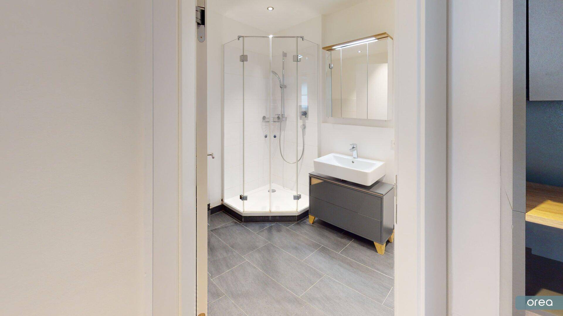 Modernes Badezimmer mit Eckdusche, Einzelwaschbecken und grauen Bodenfliesen.