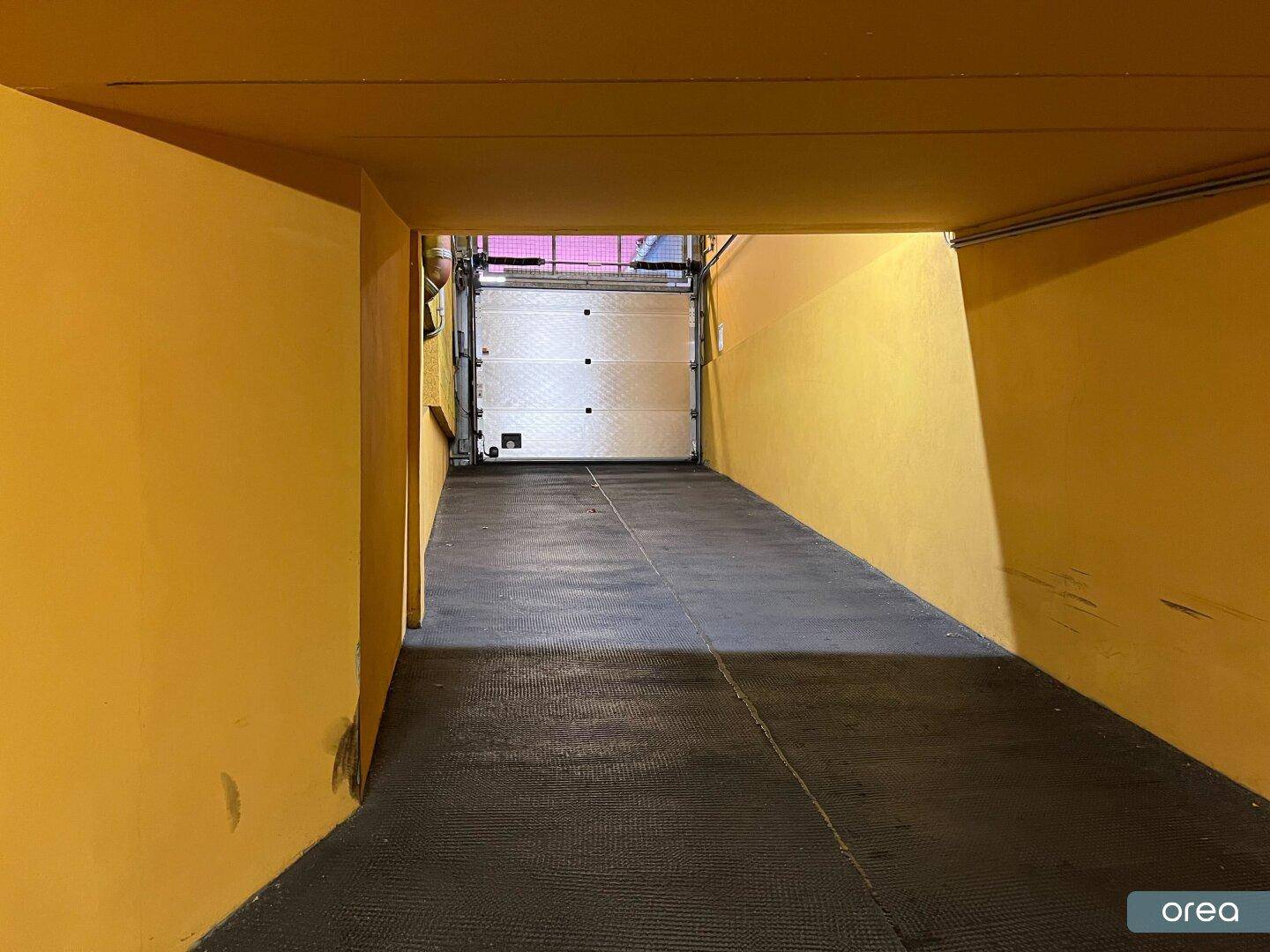 Zufahrt zur Tiefgarage mit gelben Wänden und einem geschlossenen Garagentor am Ende des Ganges.