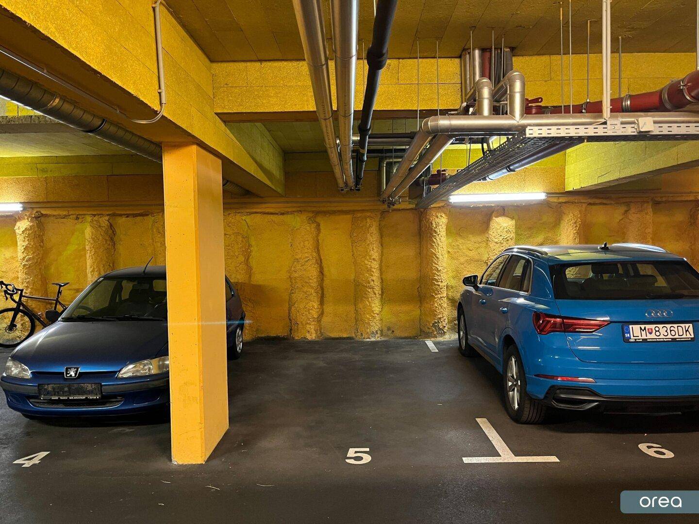 Detailansicht der Tiefgarage mit markierten Stellplätzen und gelb gestrichenen Wänden und Säulen.