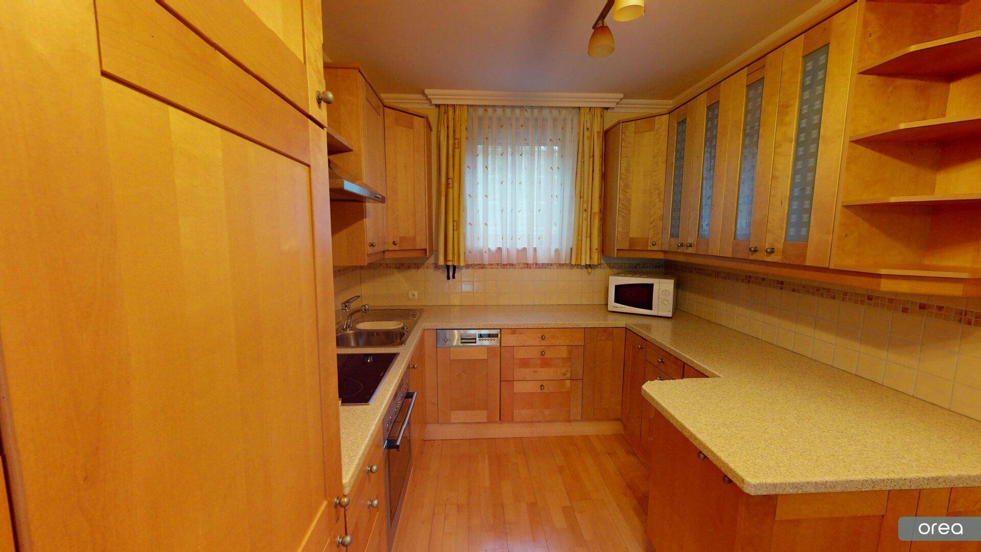 Funktionale Küche mit Holzschränken, Arbeitsflächen und integrierten Geräten.