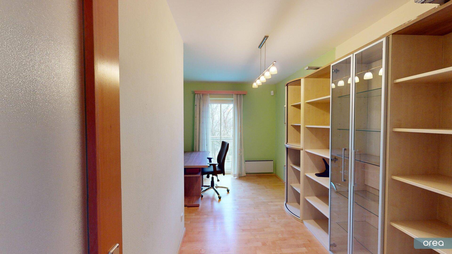 Arbeitszimmer mit Regalen, Schreibtisch und Fenster mit Blick ins Grüne.