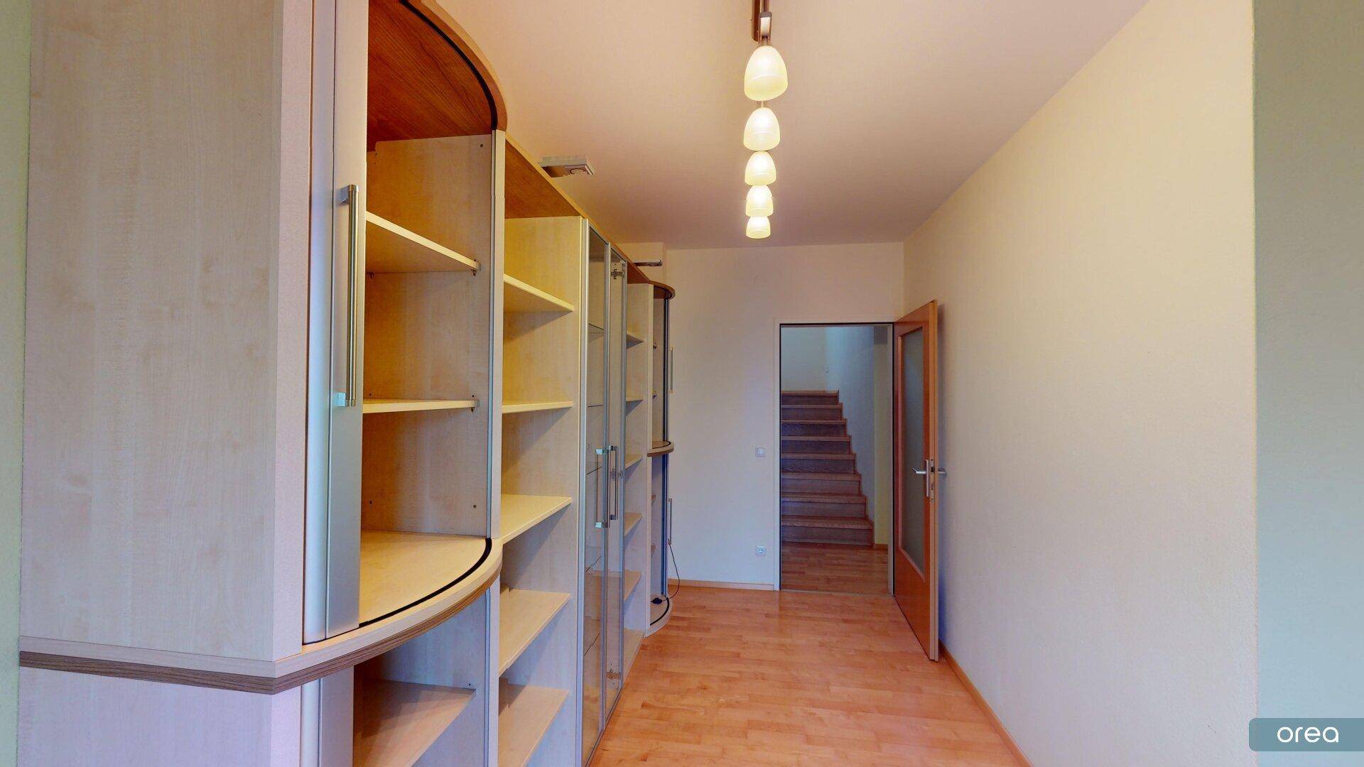 Heller Flur mit Einbauregalen und Zugang zu den oberen Etagen über eine Holztreppe.