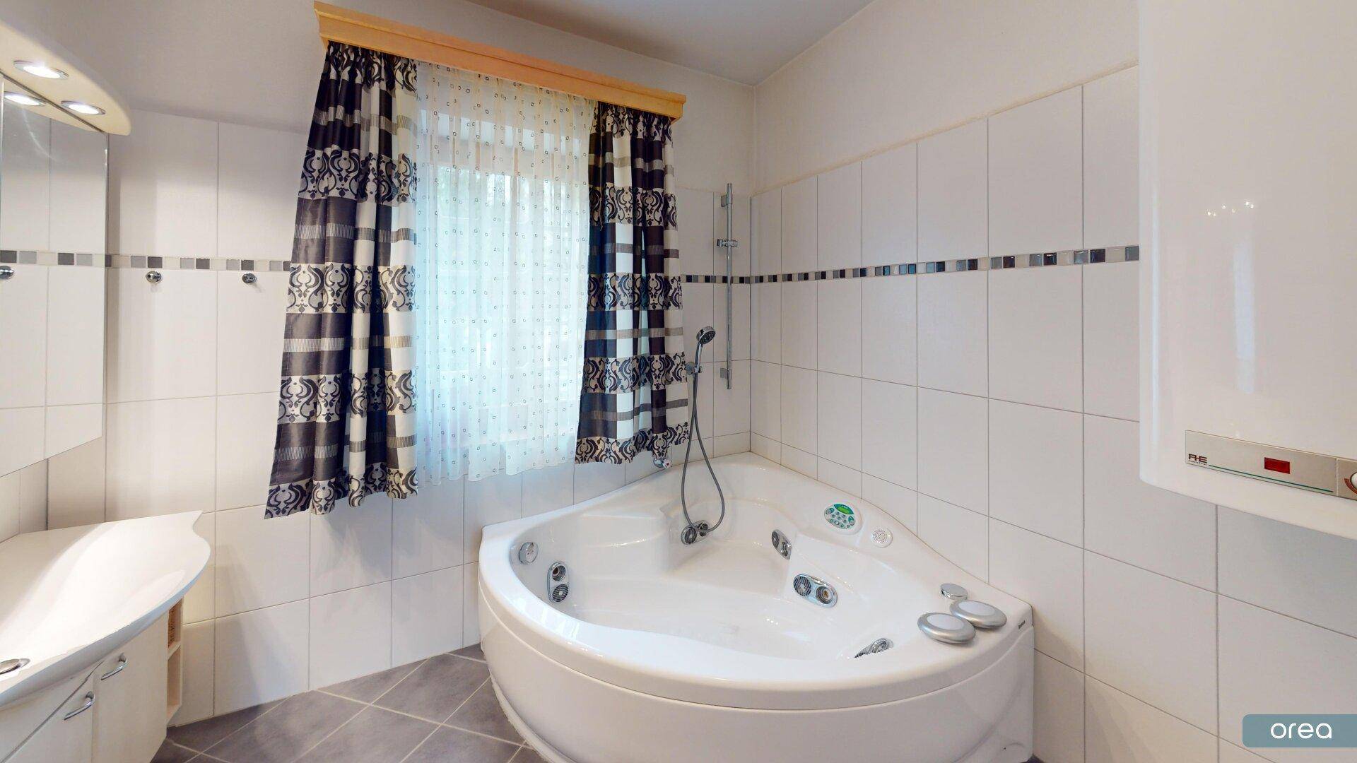 Badezimmer mit Eck-Whirlpool, Fliesen und Fenster für Tageslicht.