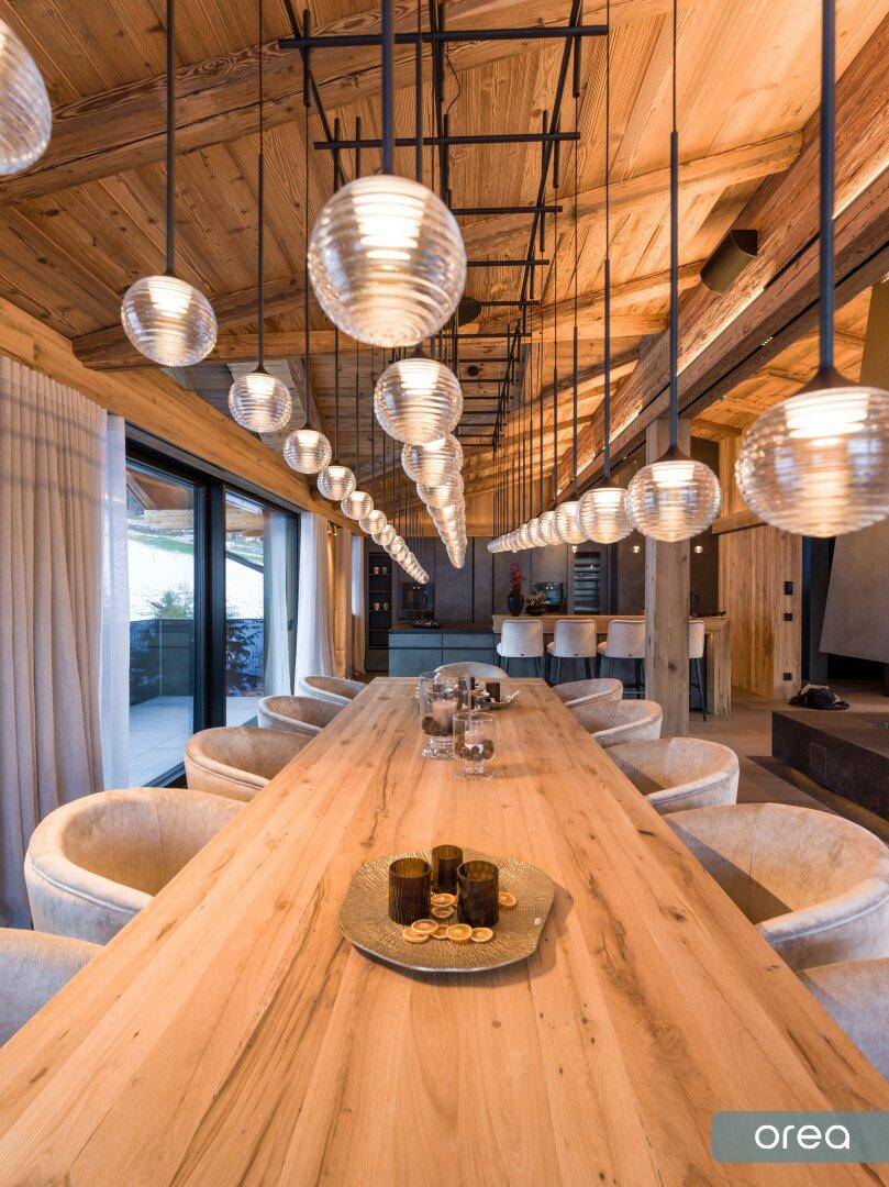 Eleganter Essbereich mit langem Holztisch, modernen Hängelampen und Blick auf die umliegende Landschaft.