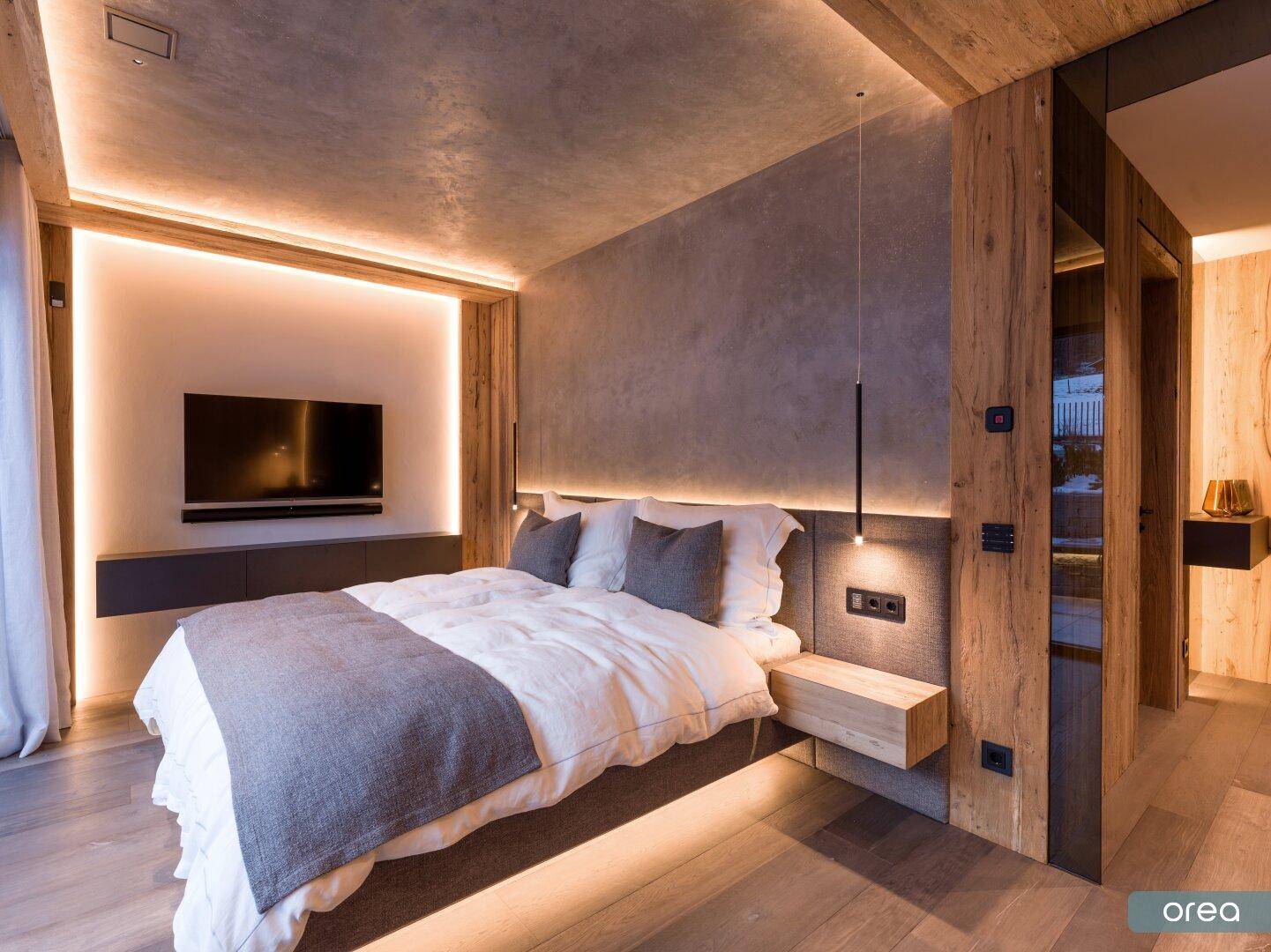 Modernes Schlafzimmer mit Holzboden, indirekter Beleuchtung und integriertem TV-Bereich.
